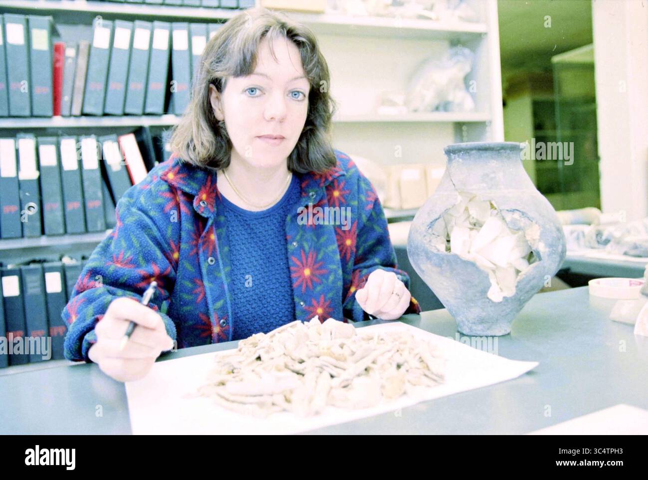Liesbeth Smits, Institute [for] Prehistory, A'Dam, Amsterdam, Paesi Bassi, 17-04-1997 Whizgle News, Dutch Desk, Paesi Bassi, 1950-2000 Una donna siede a un tavolo, esaminando e organizzando con attenzione una collezione di manufatti, tra cui frammenti di ossa e un vaso di ceramica. Dietro di lei, gli scaffali pieni di scatole di stoccaggio suggeriscono un ambiente incentrato sulla ricerca o l'archeologia. Sembra concentrata e impegnata nel suo lavoro. Foto Stock