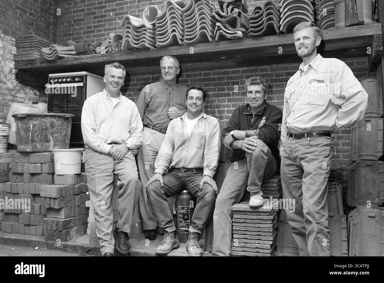 Contractors Van der Peet, Heemskerk, Van der W@@p 100 anni, Heemskerk, 22-09-1996 Whizgle News, Dutch Desk, Paesi Bassi, 1950-2000 Un gruppo di cinque uomini si trova insieme in un'officina piena di mattoni e utensili, dando prova di un senso di cameratismo. Alcuni sono seduti mentre altri si appoggiano casualmente su uno scaffale rivestito con stampi in ceramica, trasudando un'atmosfera rilassata e amichevole. Foto Stock