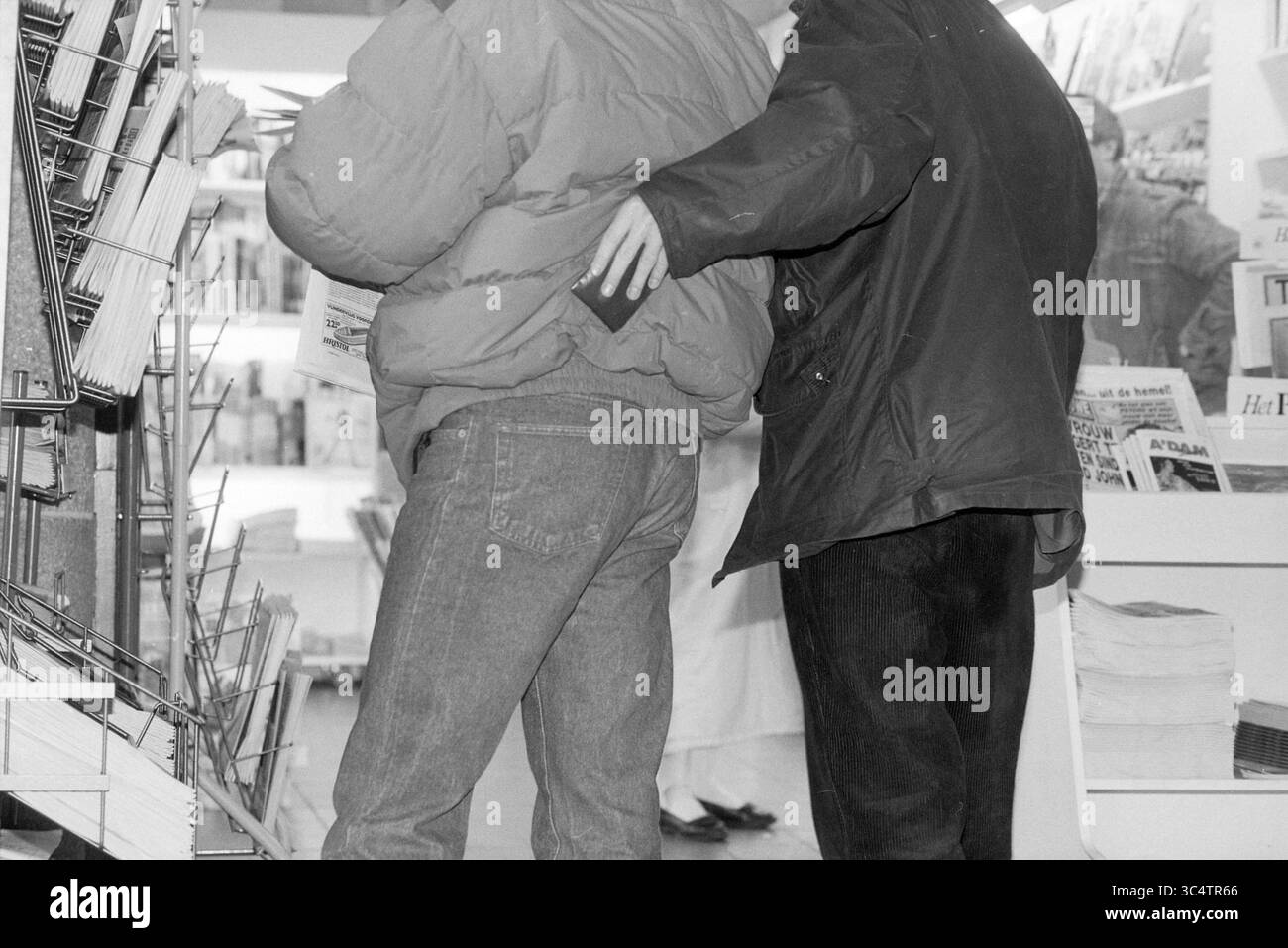 Pickpocket, stazione di Haarlem, Haarlem, Paesi Bassi, 02-05-1991 Whizgle News, Dutch Desk, Paesi Bassi, 1950-2000 due persone sono posizionate a stretto contatto in un negozio, con un uomo che si avvicina alla tasca posteriore dell’altro. Intorno a loro ci sono scaffali pieni di riviste e opuscoli, mentre un passante può essere visto sullo sfondo. Foto Stock