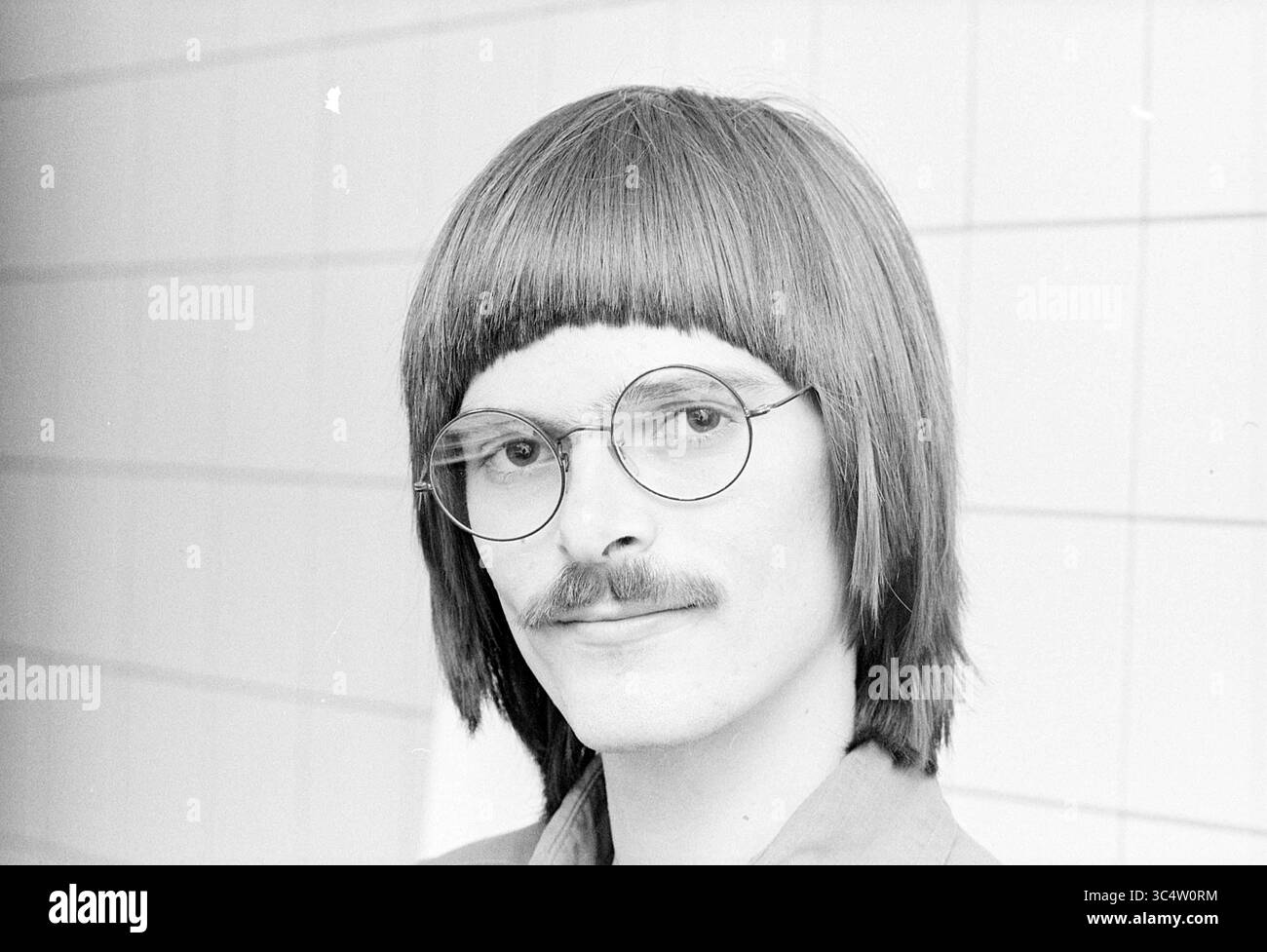 Ritratto Mr. Bakker e Robert Bakker e Jan Scheers progressive Velsen, Politics, People Politics, 08-05-1978 Whizgle News, Dutch Desk, i Paesi Bassi, 1950-2000 Un giovane con un taglio di capelli unico, bicchieri rotondi e baffi sottili sorride alla macchina fotografica, trasudando un fascino retrò. La sua espressione sicura si integra con uno sfondo semplice, mettendo in risalto il suo stile distinto. Foto Stock