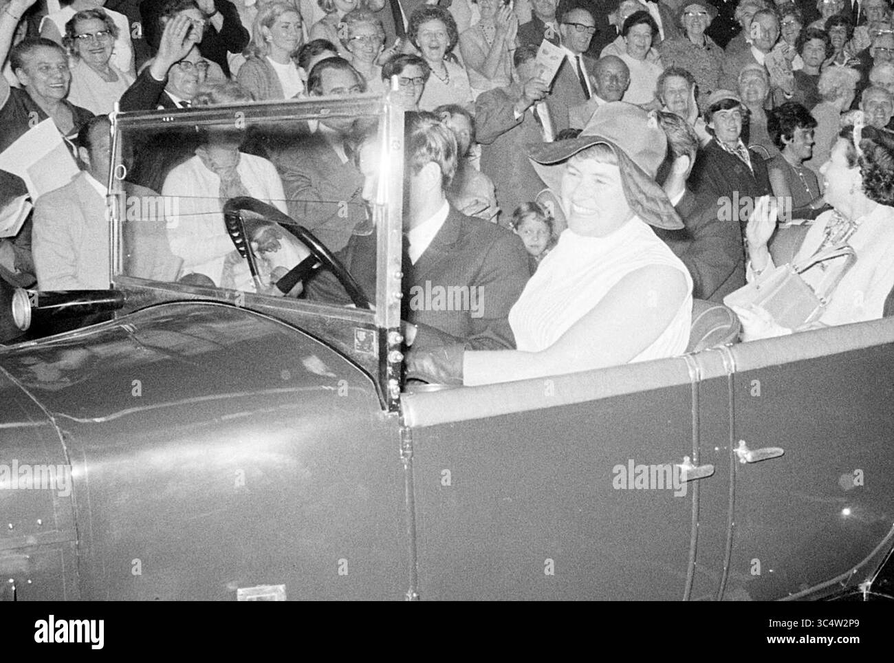 Addio burg. Cremers Sports Hall, Mayors, 30-05-1969 Whizgle News, Dutch Desk, Paesi Bassi, 1950-2000 Una donna sorridente che indossa un grande cappello siede su un'auto d'epoca, circondata da una folla entusiasta che sventola bandiere e si gode il momento. Foto Stock