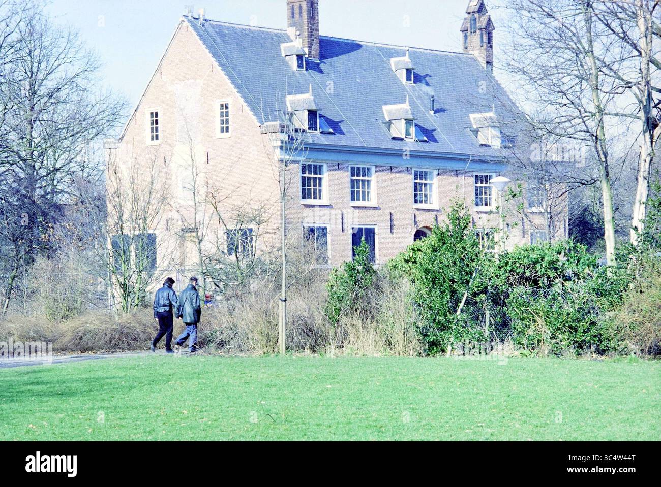 Casa a Zaanen, 16-02-1994 Whizgle News, Dutch Desk, Paesi Bassi, 1950-2000 due persone passeggiano lungo un sentiero vicino a una grande casa storica in mattoni circondata da vegetazione e alberi ricoperti. Il paesaggio presenta un lussureggiante prato verde in primo piano, in contrasto con l'architettura della casa. Foto Stock