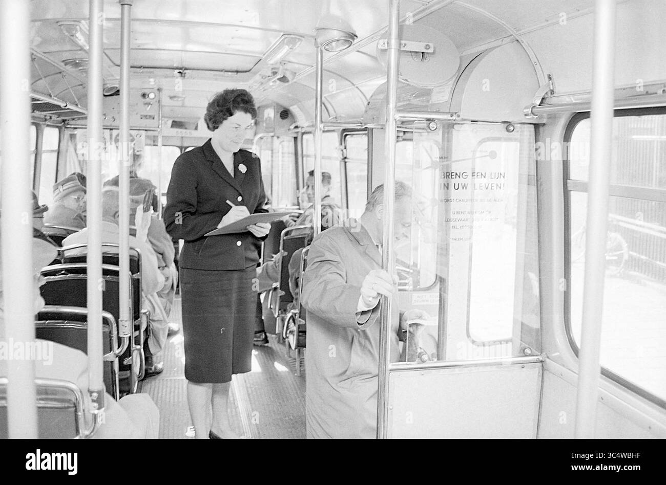 N.Z.H. Survey in the City bus, Noord Zuid Hollandse Vervoersmaatschappij N.V., NZ, 19-10-1965 Whizgle News, Dutch Desk, Paesi Bassi, 1950-2000 Una donna con un abito su misura regge un portadocumenti, mentre un uomo con un cappotto si appoggia contro un palo, entrambi circondati da passeggeri seduti in un ambiente di trasporto pubblico. L'atmosfera suggerisce un percorso urbano della metà del secolo. Foto Stock