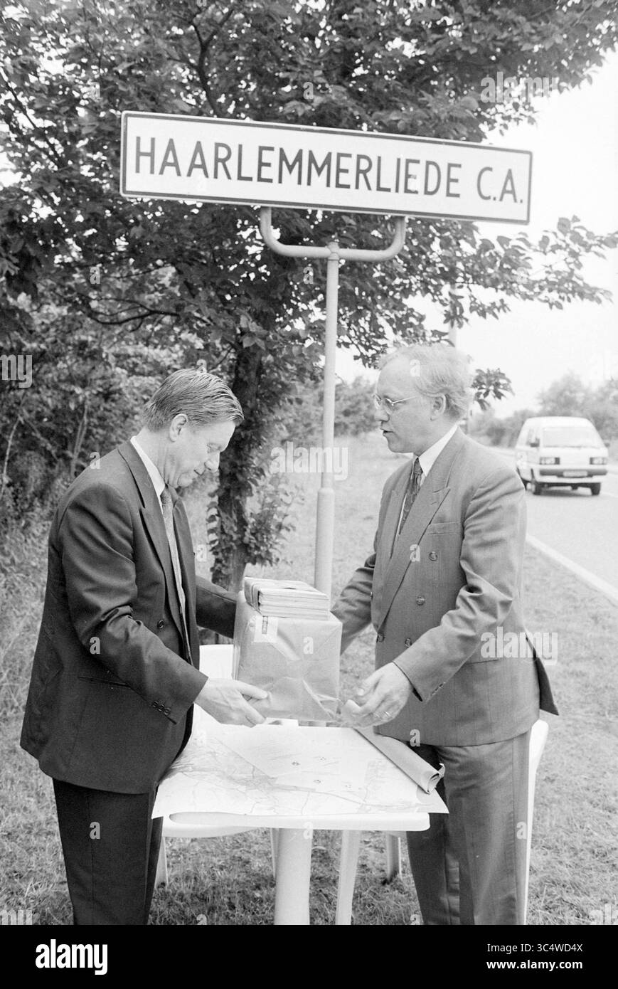T. Kruthof + Mr. Bevaart, camera di commercio, 04-07-1994 Whizgle News, Dutch Desk, Paesi Bassi, 1950-2000 due uomini in tuta si trovano su un tavolo a bordo strada, esaminando una mappa mentre sono posizionati sotto un cartello per Haarlemmerliede C.A. Un veicolo è visibile sullo sfondo, aggiungendo un tocco alla scena quotidiana. Foto Stock