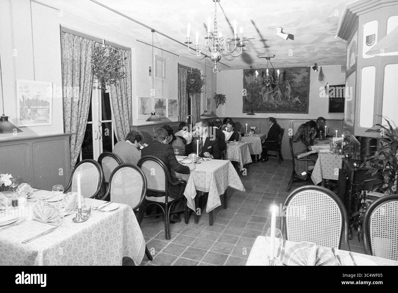 Interno del ristorante Brederodelaan 82, Bloemendaal, Bloemendaal, Brederodelaan, 28-02-1987 Whizgle News, Dutch Desk, Paesi Bassi, 1950-2000 un intimo ambiente da pranzo caratterizzato da tavoli adornati con tovaglie a motivi geometrici, dove i clienti si impegnano in conversazioni durante i pasti. L'illuminazione soffusa e il decor elegante creano un'atmosfera calda, completata da piante e decorazioni artistiche. Foto Stock