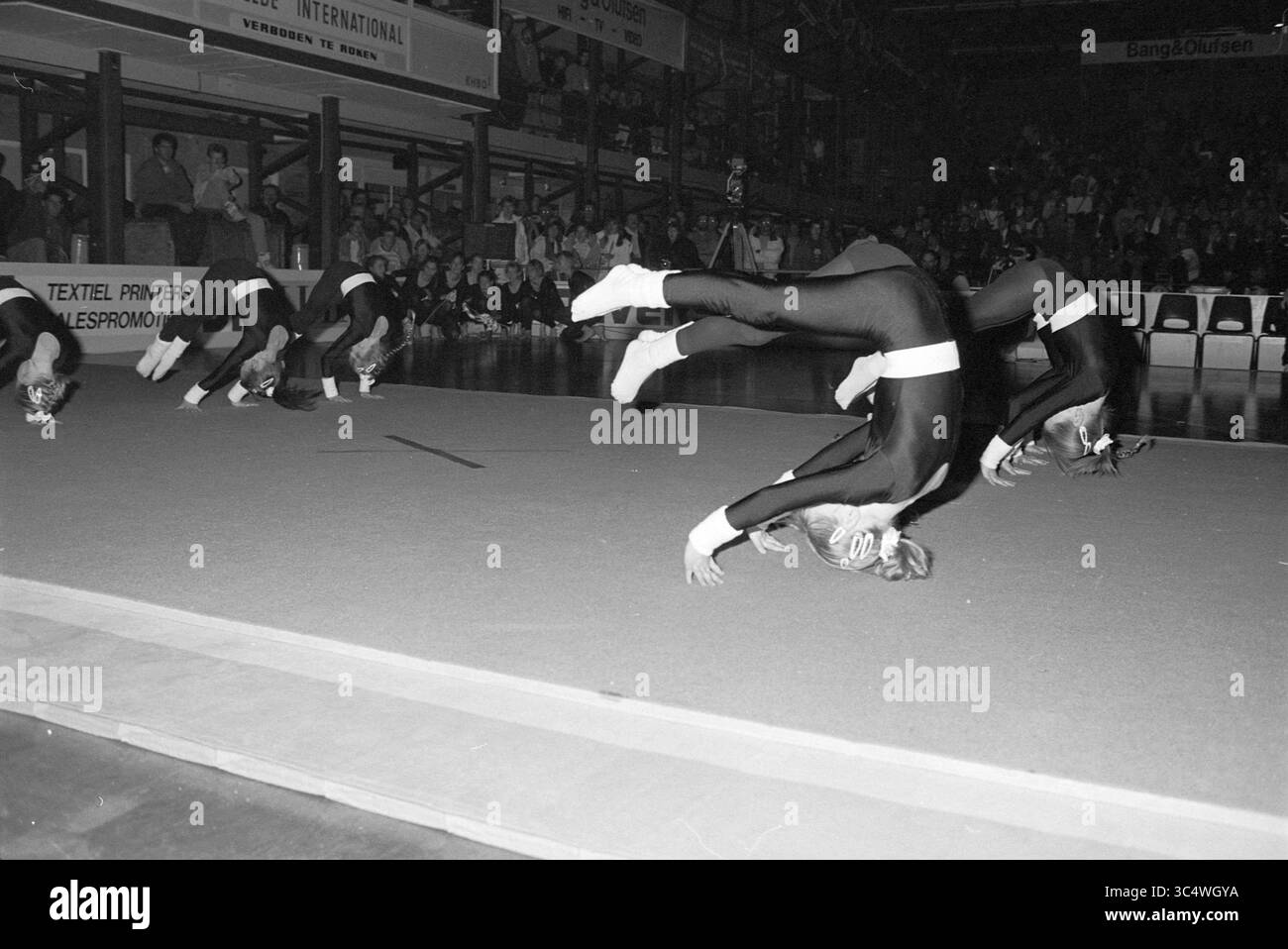Dimostrazione di ginnasti all'apertura della Basketball Week, Haarlem, Westelijke Randweg, Paesi Bassi, 21-12-1990 Whizgle News, Dutch Desk, Paesi Bassi, 1950-2000 Un gruppo di atleti esegue backflip sincronizzati su un tappetino da palestra, mostrando il loro atletismo e la loro precisione in una routine dinamica. Il pubblico in sottofondo è affascinato dalla dimostrazione di abilità e lavoro di squadra. Foto Stock