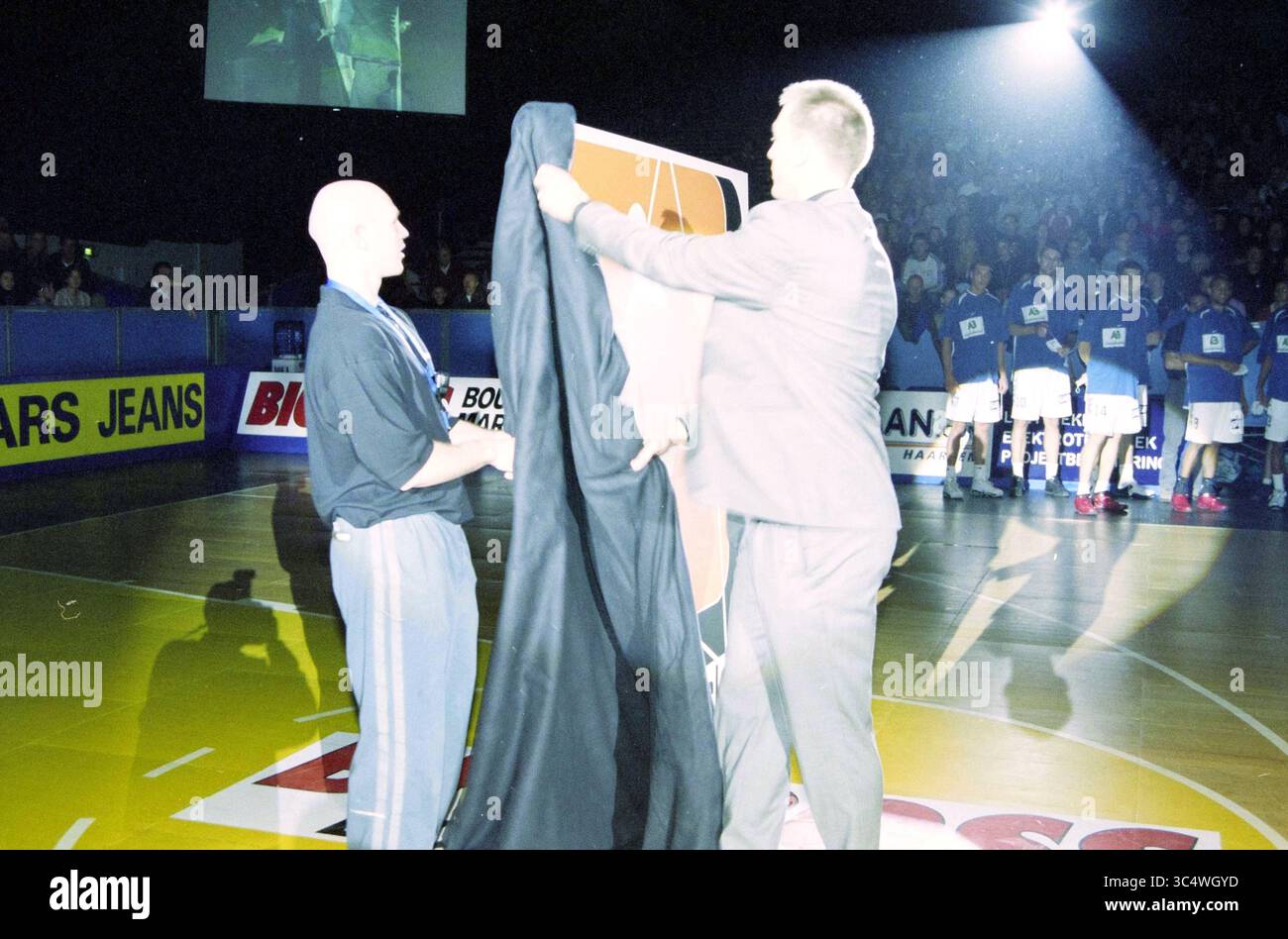 Affollato, atmosfera [Haarlem Basketball Week], 25-12-2002 Whizgle News, Dutch Desk, Paesi Bassi, 1950-2000 due persone stanno svelando un grande striscione in un evento sportivo, con una folla visibile sullo sfondo. L'attenzione è rivolta ai momenti di attesa, in quanto il banner, probabilmente associato a un team o a un evento, sta per essere completamente rivelato. Foto Stock