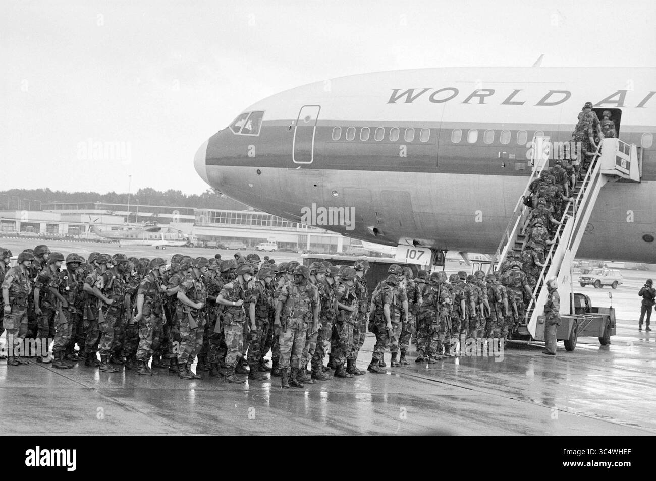 Gli americani sbarcano a Schiphol a causa di un ufficiale della forza esercitata, militare, 26-08-1987 Whizgle News, Dutch Desk, Paesi Bassi, 1950-2000 Un grande gruppo di soldati in uniformi mimetiche si allinea ai piedi di un aereo passeggeri, con altri che si imbarcano attraverso una scala vicina. La scena cattura un momento di mobilitazione militare, enfatizzando la disciplina e la prontezza mentre si preparano alla partenza. Foto Stock