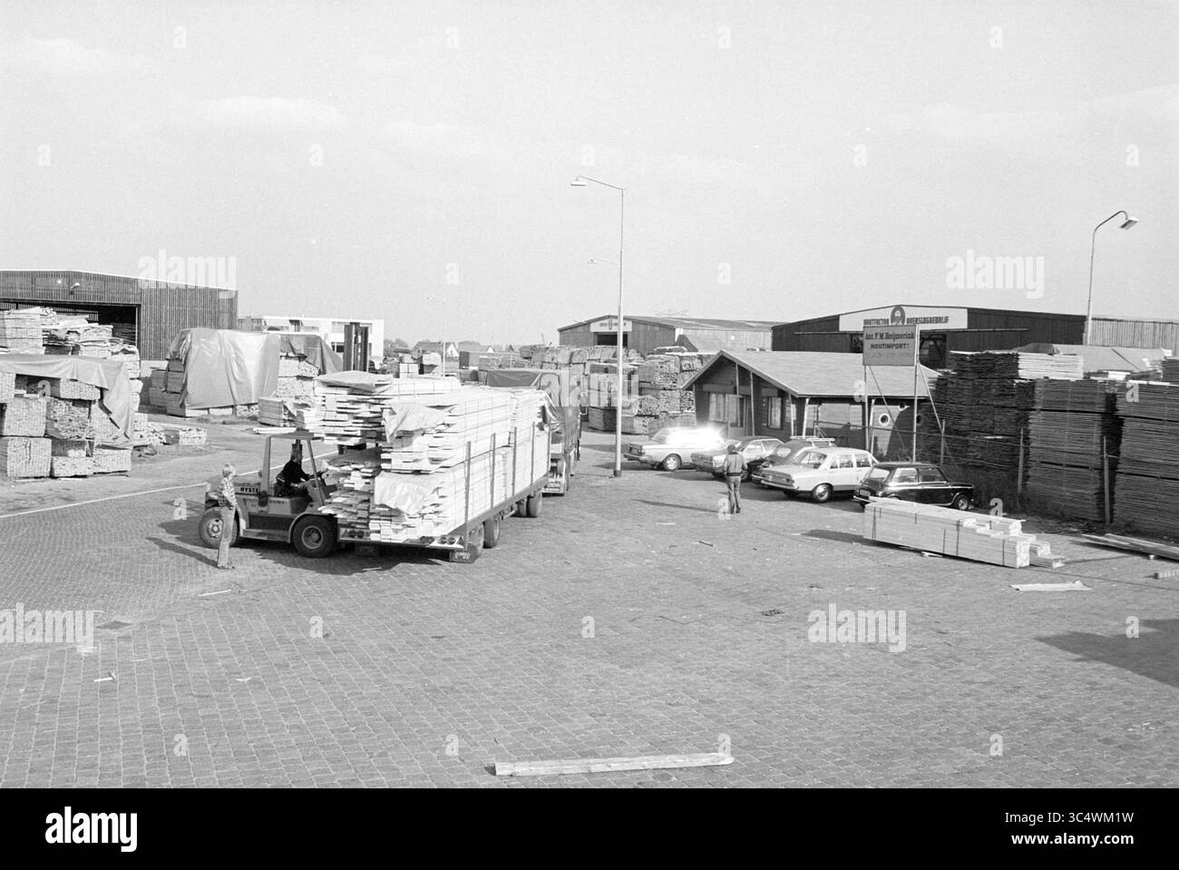 Wood Transshipment Beverwijk, Hout, Beverwijk, Paesi Bassi, 03-10-1980 Whizgle News, Dutch Desk, Paesi Bassi, 1950-2000 Un affollato cantiere di legname con pila di legno e compensato, con veicoli parcheggiati nelle vicinanze. I lavoratori vengono visti scaricare materiali da un camion, mentre edifici e pile di pannelli di legno formano lo sfondo. Foto Stock