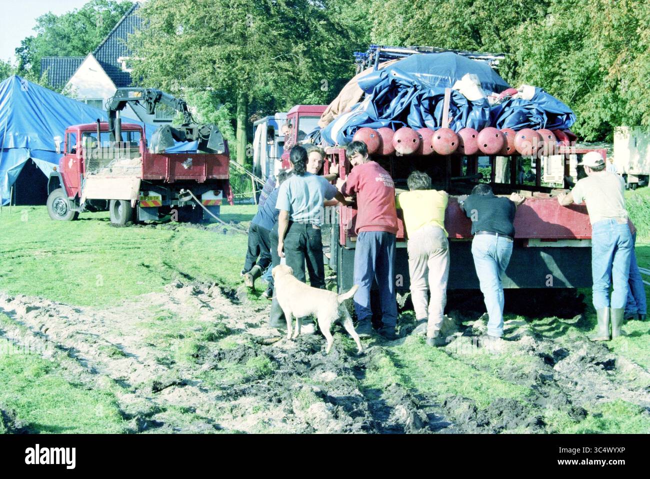 Installazione di tende da circo, Heemstede, Heemstede, Paesi Bassi, 09-09-1998 Whizgle News, Dutch Desk, Paesi Bassi, 1950-2000 Un gruppo di persone lavora insieme per spingere un grande camion bloccato su un terreno fangoso, mentre un cane osserva nelle vicinanze. Le tende sono disposte sullo sfondo, indicando un evento o una riunione all'aperto. Foto Stock