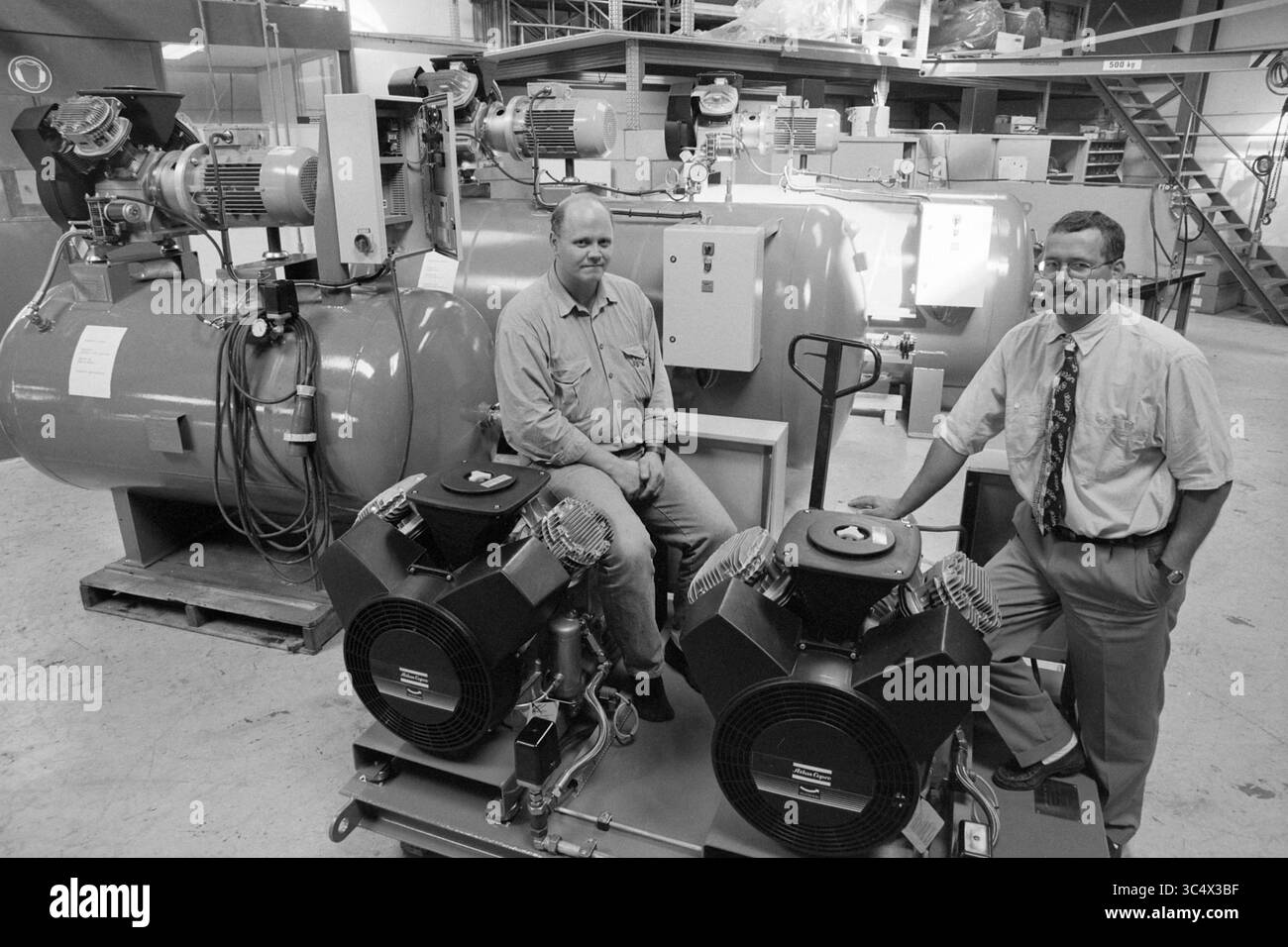 Signor Vis, Ketting, IJm., IJmuiden, Paesi Bassi, 08-09-1996 Whizgle News, Dutch Desk, Paesi Bassi, 1950-2000 due persone si trovano accanto alle apparecchiature industriali in un'officina, con vari macchinari e compressori sullo sfondo. Sembra che stiano discutendo o dimostrando le attrezzature, dimostrando la loro esperienza sul campo. Foto Stock