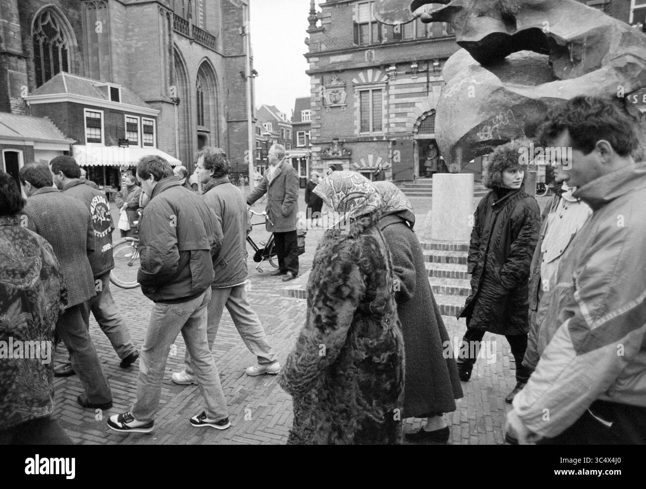 Dimostrazione a Haarlem di rifugiati bosniaci provenienti da centri di accoglienza nei Paesi Bassi contro la violenza della guerra e la violazione dei diritti umani in Bosnia. Chiedono anche che i criminali di guerra siano portati davanti a un tribunale internazionale., Haarlem, Grote Markt, Paesi Bassi, 20-02-1993 Whizgle News, Dutch Desk, Paesi Bassi, 1950-2000 Una vivace scena urbana presenta un gruppo diversificato di persone che camminano davanti a una grande scultura astratta. L'architettura degli edifici vicini aggiunge un carattere storico all'ambiente, mentre gli individui espongono stili di moda diversi, evidenziando un momento di ev Foto Stock