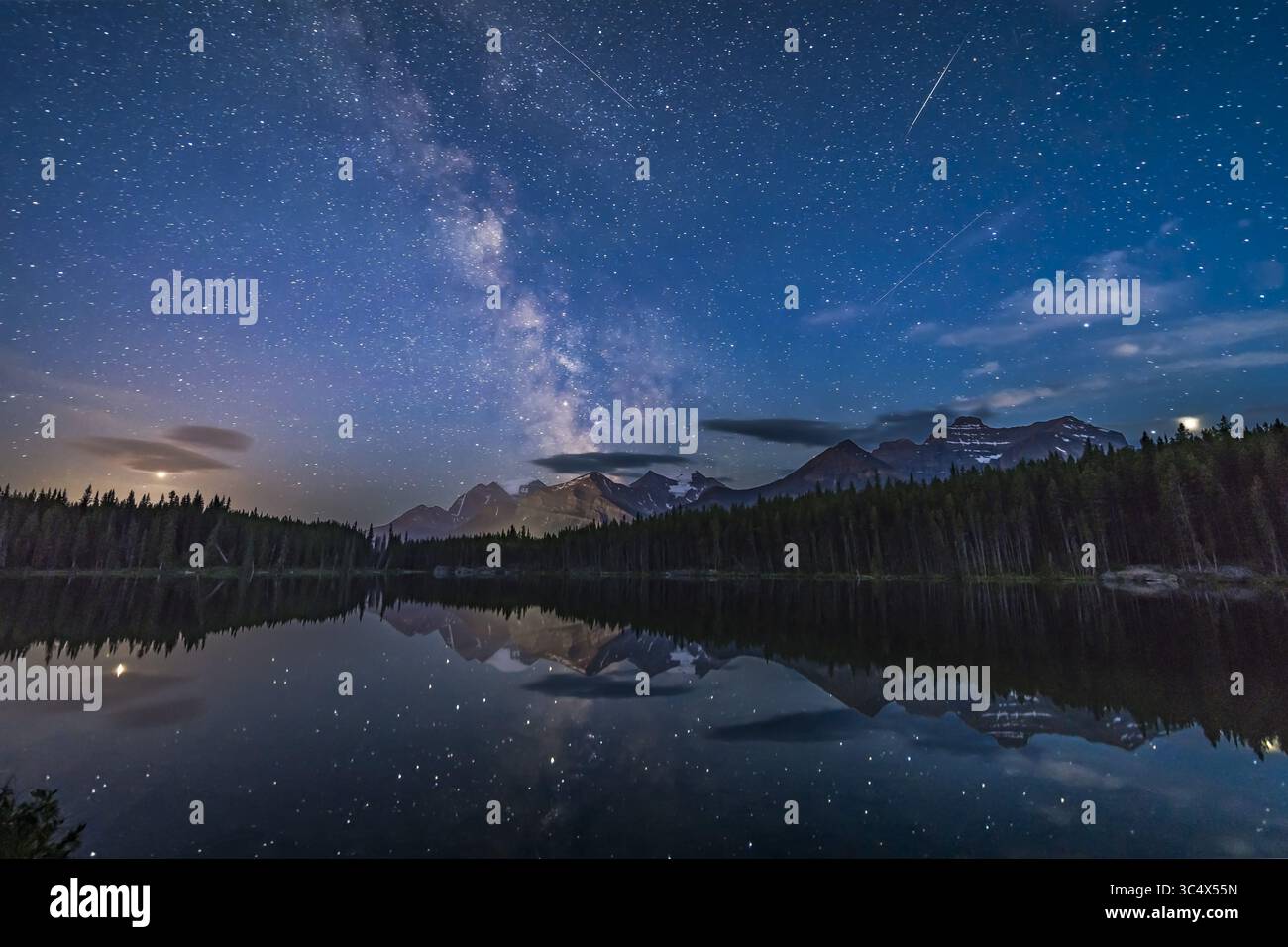 18 luglio 2018 - Alberta, Canada - la vista a sud del lago Herbert, del Parco Nazionale di Banff, Alberta, con la via Lattea sul Monte Temple e le vette del Continental divide. Marte (a sinistra tra le nuvole) e Giove (a destra) fiancheggiano la via Lattea, mentre Saturno si trova all'interno della via Lattea. Anche un paio di satelliti e forse una meteora (potrebbe essere un satellite che esplode) punteggiano il cielo. ..il cielo è blu con le ultime vestigia del crepuscolo e dal chiaro di luna dall'ambientazione che fa sprofondare la Luna fuori dalla cornice a destra. Si tratta di quattro esposizioni per la media del terreno combinate con un rumore uniforme e un'esposizione Foto Stock