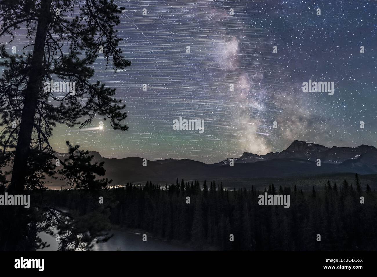 15 luglio 2018 - Alberta, Canada - le stelle si spostano da est a ovest (da sinistra a destra), terminando con la via Lattea e il Centro Galattico (a destra) sopra Storm Mountain e l'area del passo Vermilion del Continental divide nel Banff National Park, Alberta. Marte è la pista luminosa a sinistra. Saturno è in mezzo alla via Lattea a destra. Era il 15 luglio 2018. Le luci a sinistra provengono dallo svincolo Castle Mountain sulle autostrade 1 e 93... si tratta di una pila di 8 esposizioni, media combinata per un rumore uniforme, per il terreno, più 200 esposizioni per i sentieri stellari, e una esposizione, non tracciata, per il fisso Foto Stock