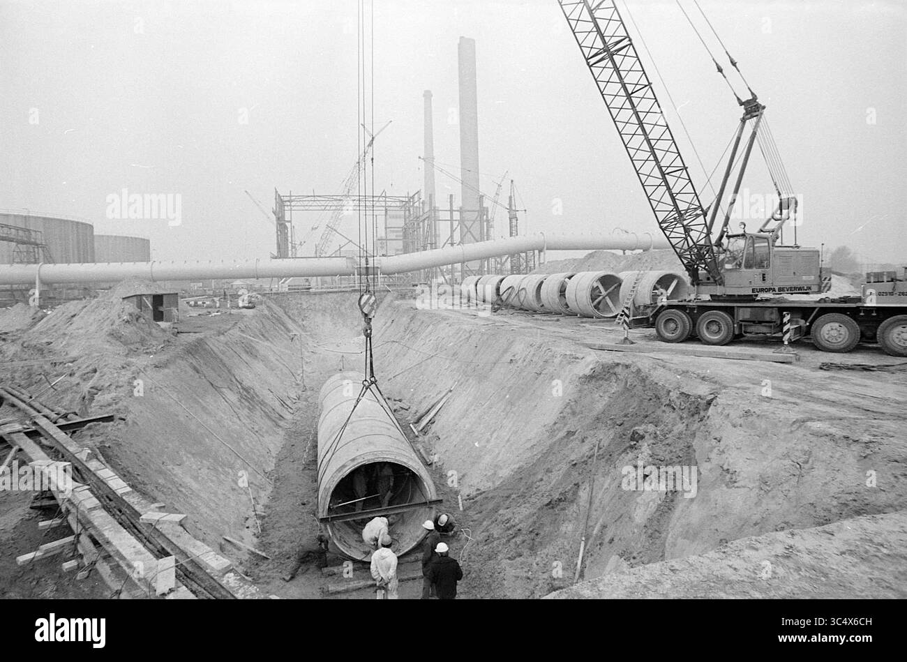 Posa di tubi Velsen., Work, 24-02-1972 Whizgle News, Dutch Desk, Paesi Bassi, 1950-2000 Un cantiere con tubi di grandi dimensioni installati con l'aiuto di una gru, mentre gli operatori osservano il processo. In background, sono visibili strutture e attrezzature edili in corso, a indicare un progetto industriale significativo. Foto Stock