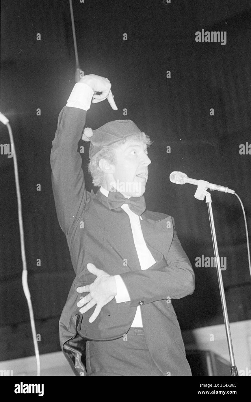 50th Anniversary of CBR, party staff, C.B.R., 08-10-1977 Whizgle News, Dutch Desk, i Paesi Bassi, 1950-2000 Un artista in un abito da smoking e cravatta colpisce una posa espressiva tenendo in mano un microfono, coinvolgendo il pubblico con gesti animati e un'espressione giocosa. Foto Stock