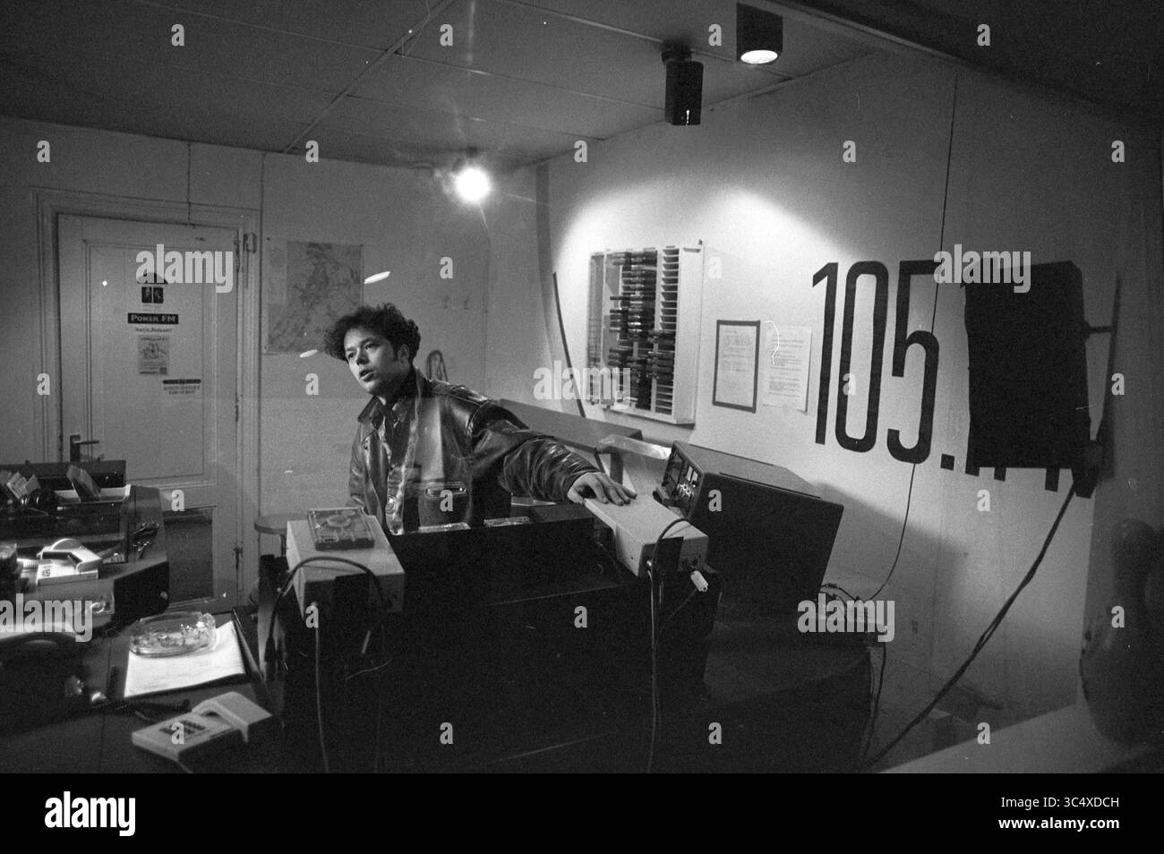 Presentatore nello studio radio Haarlem. 105.1FM, Haarlem, Paesi Bassi, 01-04-1992 Whizgle News, Dutch Desk, i Paesi Bassi, 1950-2000 persone si trovano dietro una serie di apparecchiature in un piccolo studio, con vari dispositivi audio visibili e un gran numero di "105.5" esposto sulla parete. Mappe e grafici adornano lo spazio, suggerendo un ambiente creativo o di trasmissione. L'atmosfera suggerisce un momento di concentrazione e coinvolgimento nel loro lavoro. Foto Stock