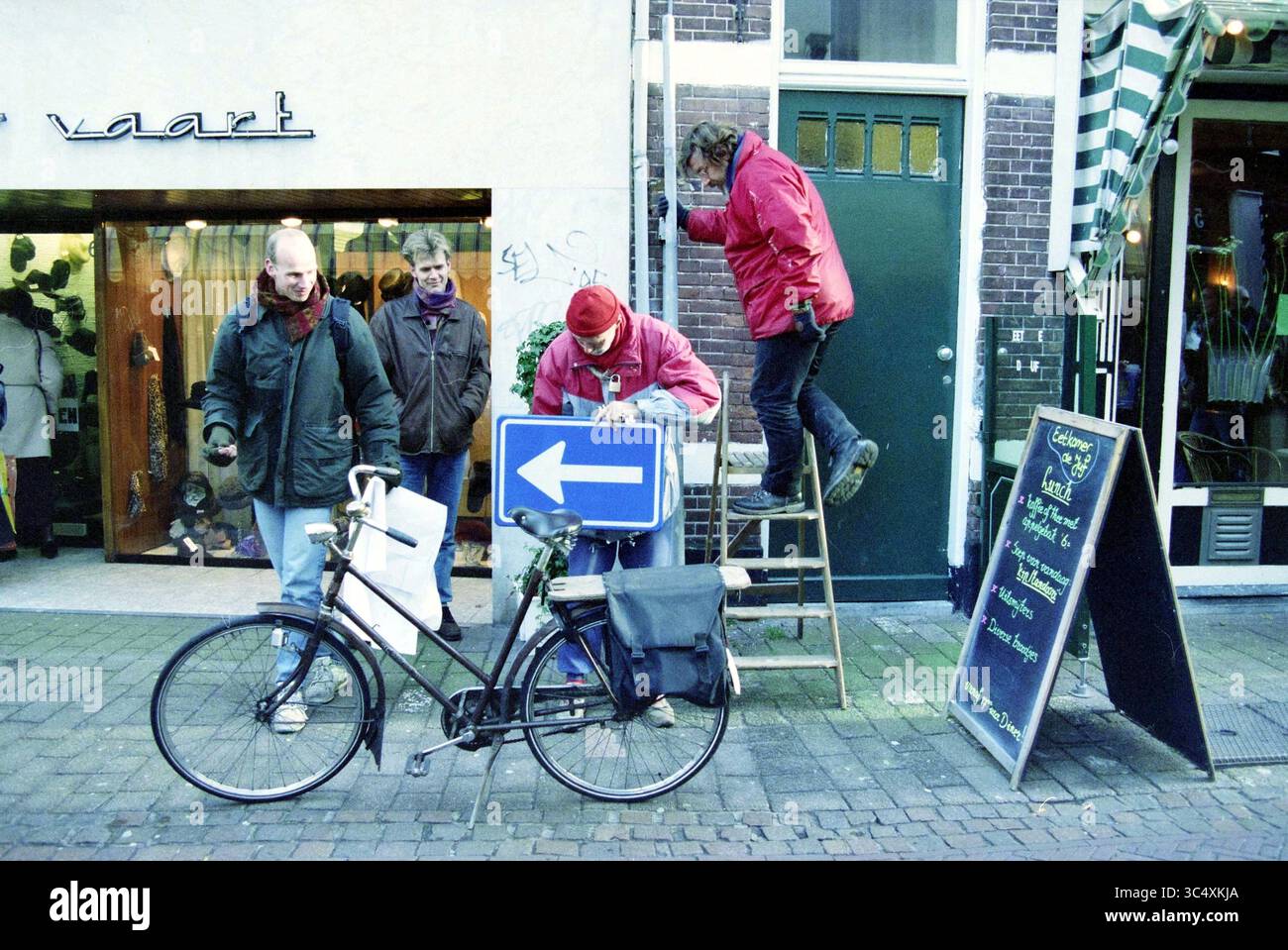Action Cyclists' Union, Gierstr., Haarlem, Gierstraat, Paesi Bassi, 13-12-1996 Whizgle News, Dutch Desk, Paesi Bassi, 1950-2000 Un gruppo di quattro persone si impegna in varie attività in una strada trafficata. Una persona sta in cima a una scala, regolando un segnale, mentre un'altra esamina un dispositivo nelle vicinanze. Altri due osservano la scena, contribuendo a creare un'atmosfera vivace. Una bicicletta è parcheggiata nelle vicinanze, aggiungendo un tocco di fascino urbano. Foto Stock