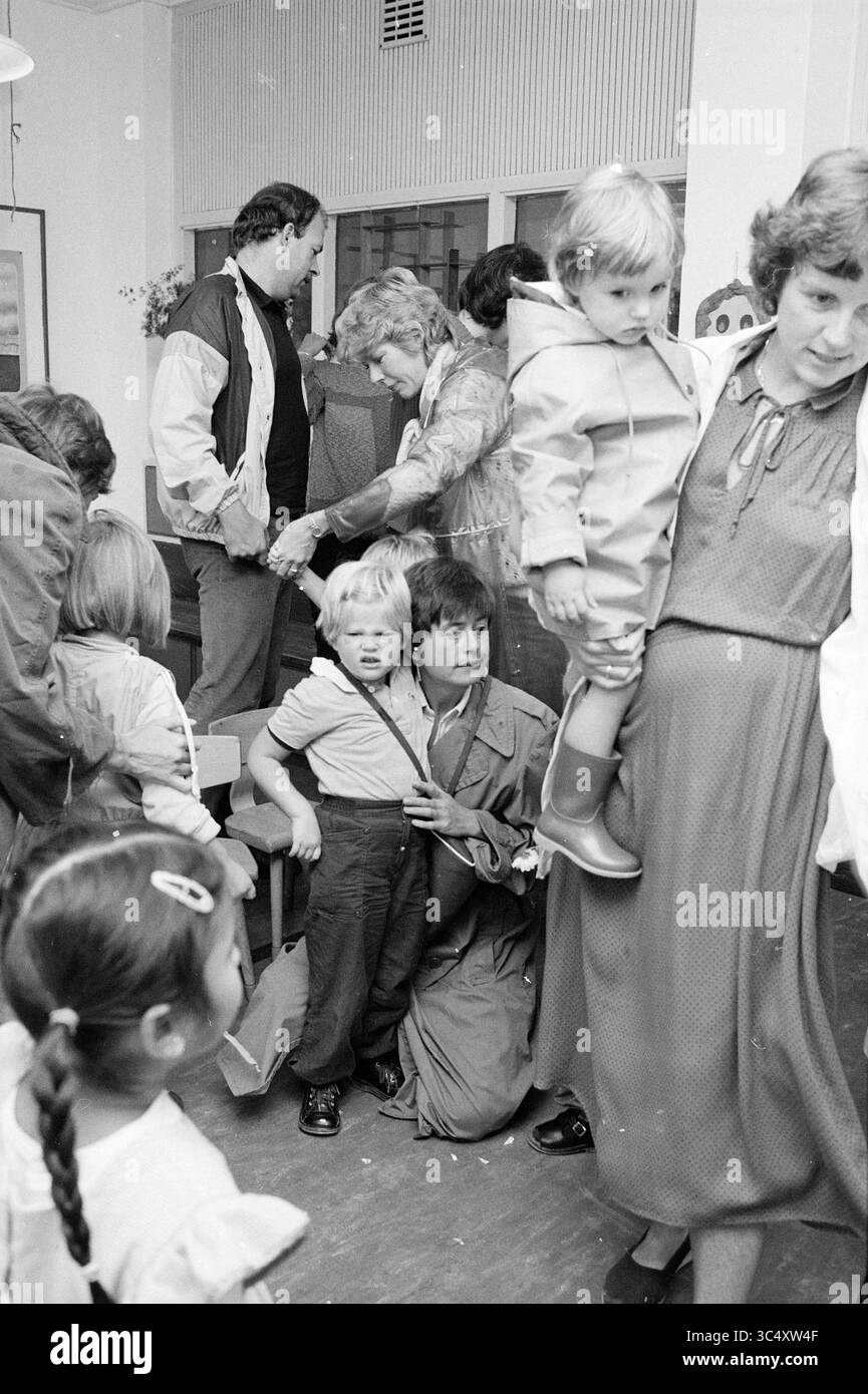 1° giorno di scuola materna terCleeff, scuole, 22-08-1982 Whizgle News, Dutch Desk, Paesi Bassi, 1950-2000 Una camera affollata piena di persone, compresi adulti e bambini, impegnate in varie attività. Alcuni adulti interagiscono mentre i bambini giocano nelle vicinanze, creando un'atmosfera vivace. Una donna tiene un bambino mentre un altro bambino sta vicino, guardando curiosamente l'ambiente circostante. Foto Stock