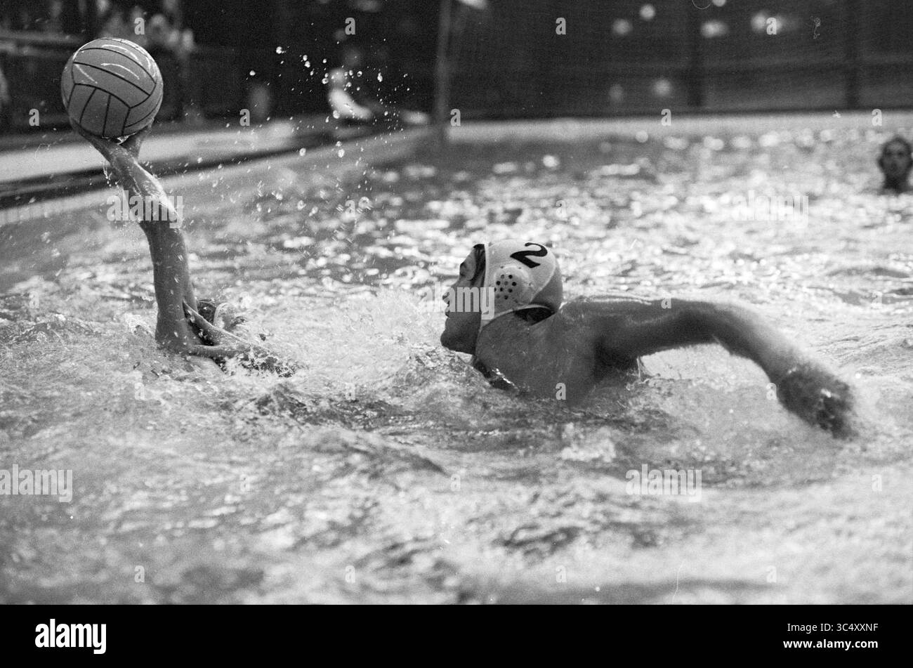 Rapido - Loser, pallanuoto, 06-10-1984 Whizgle News, Dutch Desk, Paesi Bassi, 1950-2000 Un giocatore di pallanuoto è pronto a sparare la palla mentre un altro giocatore raggiunge la difesa, creando un momento intenso in acqua. L'area circostante della piscina richiama l'atmosfera competitiva dello sport. Foto Stock