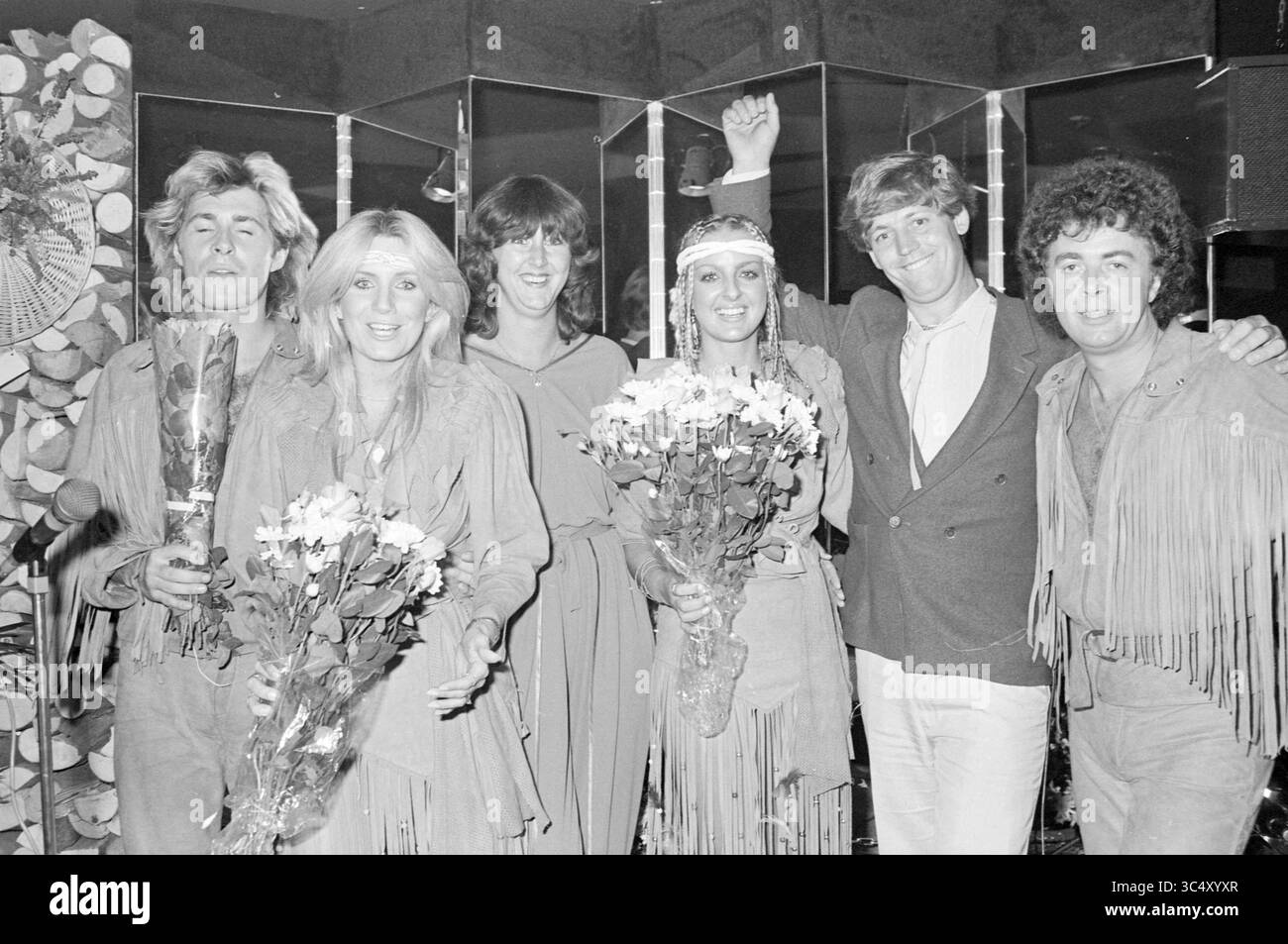 Spettacolo Guys 'n' Dolls al Club Cartier, Haarlem, Paesi Bassi, 23-07-1982 Whizgle News, Dutch Desk, i Paesi Bassi, 1950-2000 Un gruppo di sei persone vestite con abiti frangiati sorride insieme, tenendo mazzi di fiori. Sembra che stiano celebrando un successo, con una persona che alza il braccio di gioia. L'ambiente presenta pareti a specchio e un'atmosfera festosa. Foto Stock