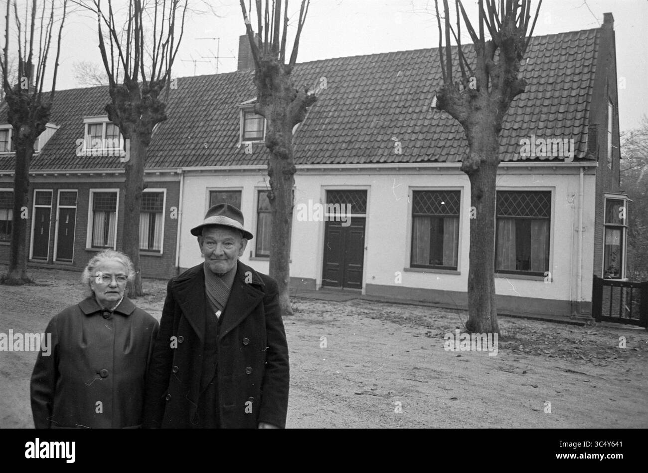 Coppia di Doesburg, vecchio addetto al parcheggio, persone, 10-11-1965 Whizgle News, sportello olandese, i Paesi Bassi, 1950-2000 una coppia di anziani si trova fianco a fianco in una strada tranquilla, circondata da alberi ben rifilati. Dietro di loro, una fila di case pittoresche presenta dettagli architettonici distinti, che mettono in risalto un'atmosfera serena e senza tempo. Foto Stock