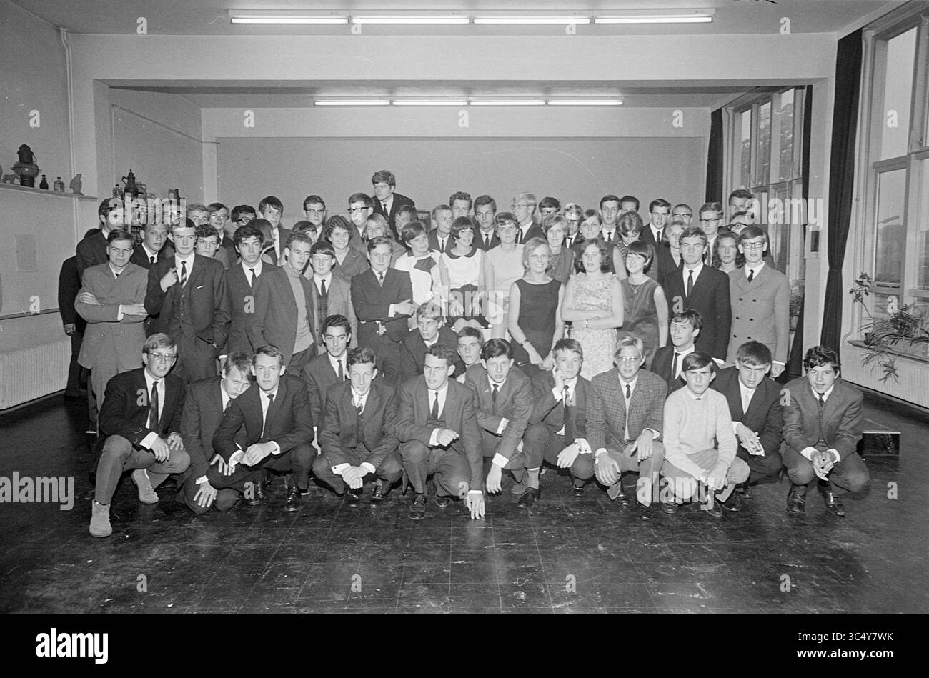Gruppo di laureati Mendel College, gruppi, 27-06-1966 Whizgle News, Dutch Desk, Paesi Bassi, 1950-2000 Un grande gruppo di studenti posa in classe, indossando un abbigliamento formale. Sono disposti in più file, con alcune sedute davanti e altre in piedi dietro. L'ambiente presenta grandi finestre e decorazioni scolastiche, creando un'atmosfera nostalgica. Foto Stock