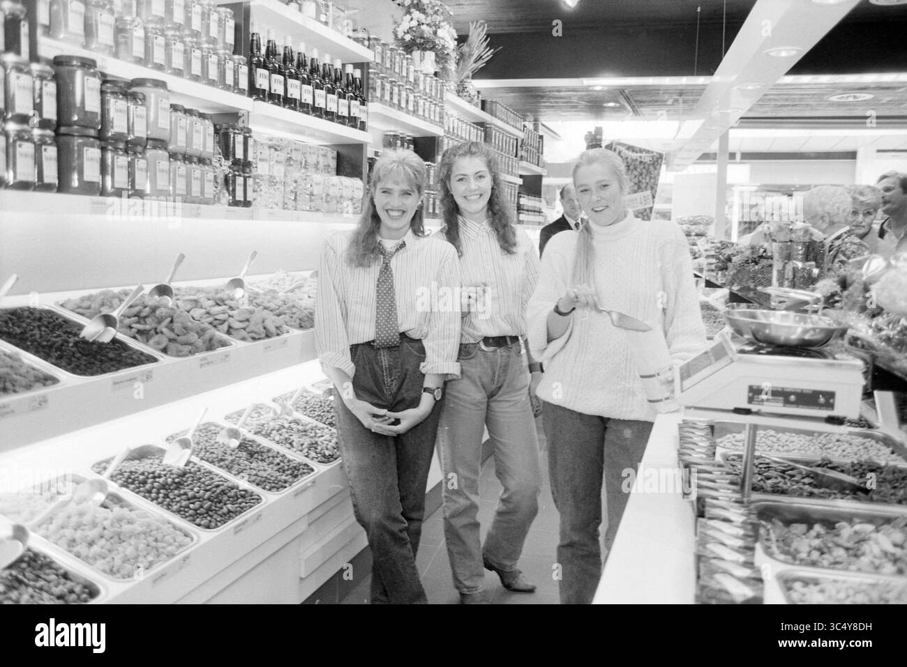 Staff C´est Bon, Schalkwijk, 25-09-1991 Whizgle News, Dutch Desk, Paesi Bassi, 1950-2000 tre donne sorridono in un vivace mercato, circondato da una serie di vasi colorati e contenitori pieni di vari alimenti, tra cui frutta secca e noci. L'atmosfera vivace suggerisce una piacevole esperienza di shopping. Foto Stock