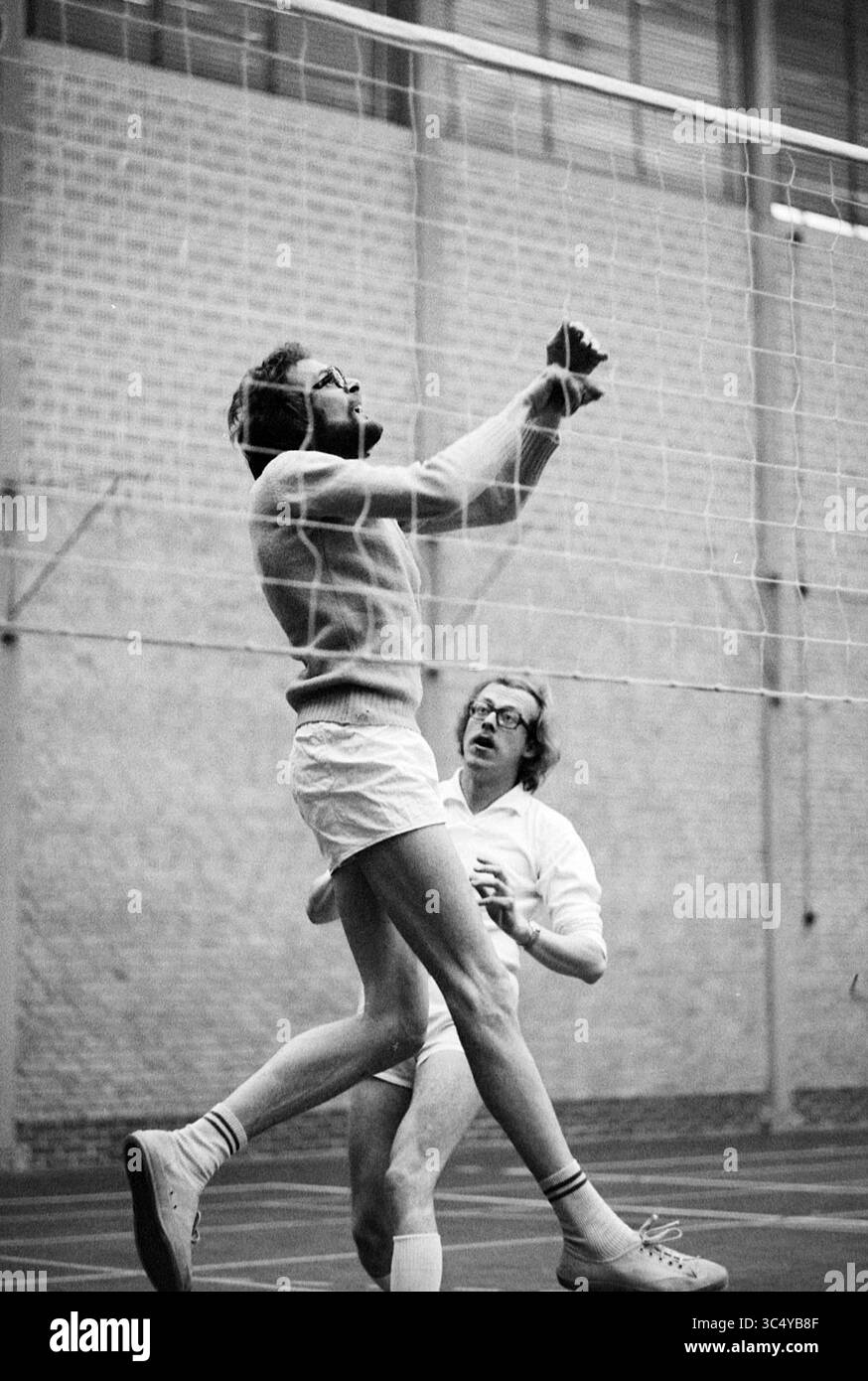 Partite di pallavolo Whizgle News, Dutch Desk, Paesi Bassi, 1950-2000 due persone sono impegnate in una partita di pallavolo. Un giocatore sta saltando per intercettare la palla vicino alla rete, mostrando atletismo e concentrazione, mentre l'altro guarda avanti, preparandosi per la mossa successiva. L'impostazione interna evidenzia l'intensità della partita. Foto Stock