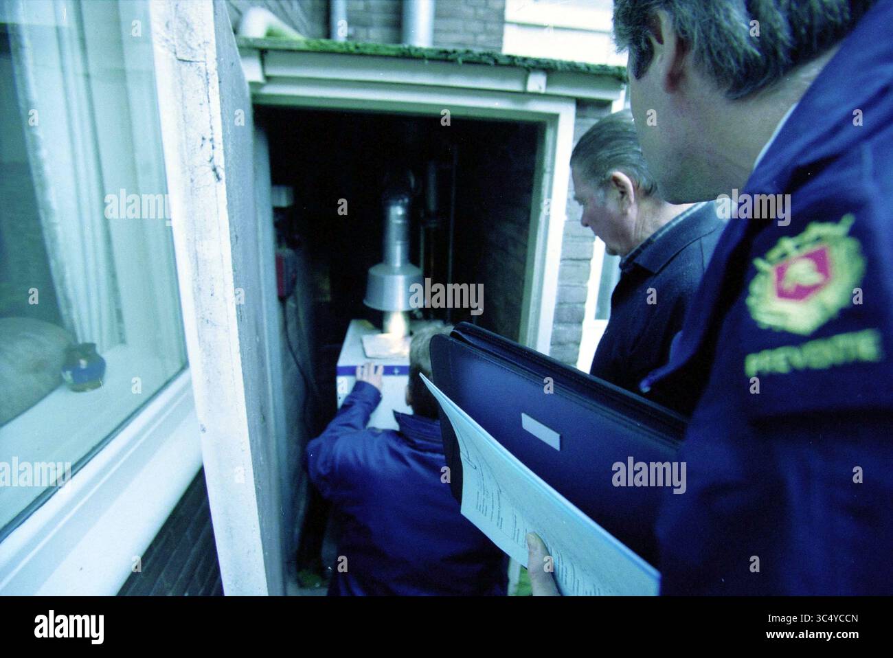 Ispezione della Snipstraat House, Badhoevedorp, Badhoevedorp, Snipstraat, 26-11-2003 Whizgle News, Dutch Desk, Paesi Bassi, 1950-2000 Un gruppo di persone osserva un tecnico che lavora su un dispositivo di pubblica utilità all'esterno di un edificio, tenendo in mano documenti e discutendo del processo di manutenzione o ispezione in corso. Foto Stock