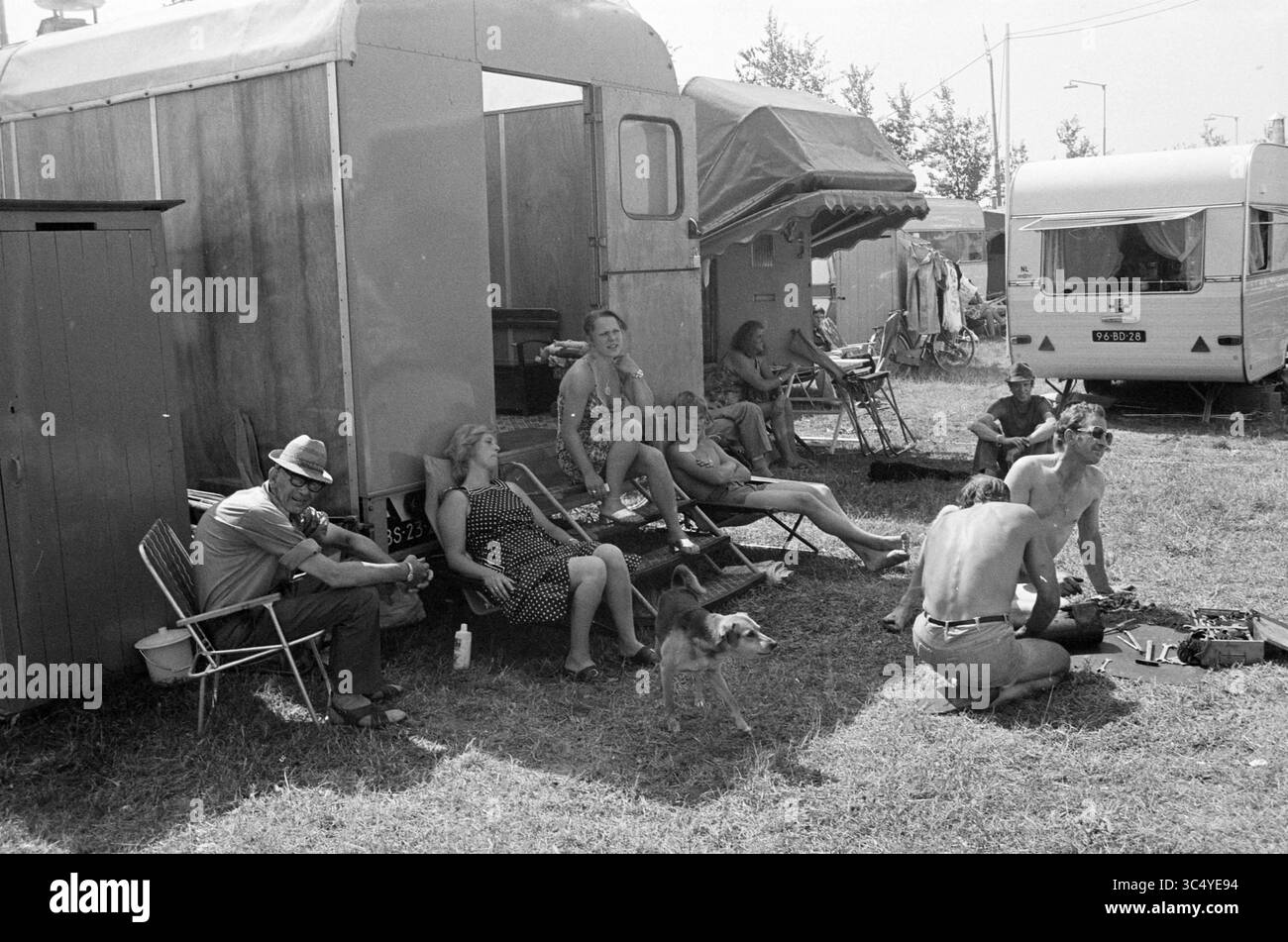 Caravan Residents Whizgle News, Dutch Desk, The Netherlands, 1950-2000 Un gruppo di persone si rilassa all'esterno dei propri rimorchi in un'area erbosa, godendosi del tempo libero insieme. Alcune sono sedute su sedie, mentre altre sono impegnate in varie attività, con un cane che vagava nelle vicinanze. La scena trasmette un senso di comunità e giornate estive informali. Foto Stock
