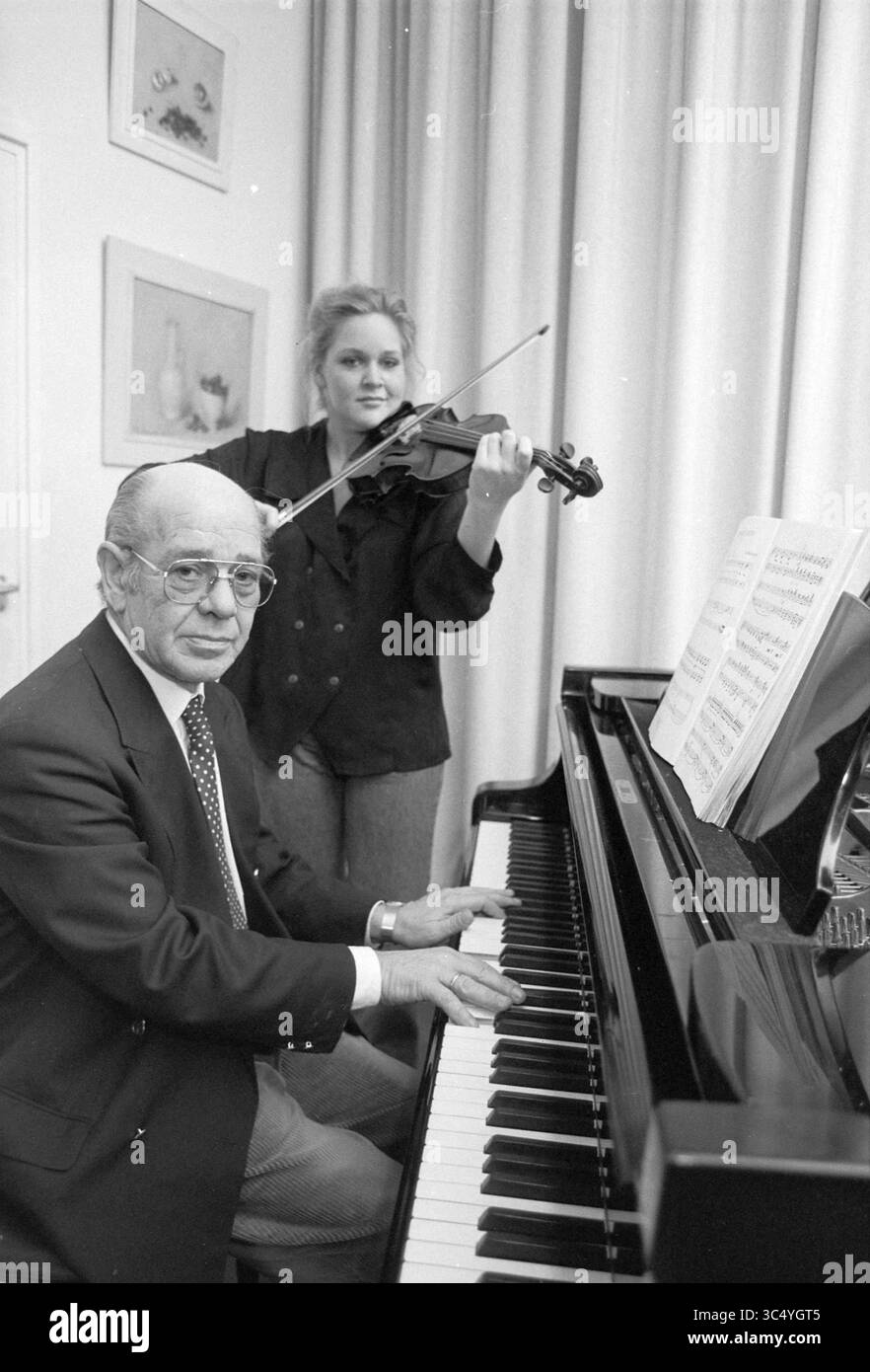 Sig. De Groot con figlia, Haarlem, Paesi Bassi, 12-11-1991 Whizgle News, Dutch Desk, i Paesi Bassi, 1950-2000 Un uomo siede al pianoforte a coda, suona, mentre una donna sta dietro di lui, suonando abilmente il violino. Gli spartiti sono aperti di fronte al pianista, creando un'atmosfera di collaborazione musicale. Foto Stock