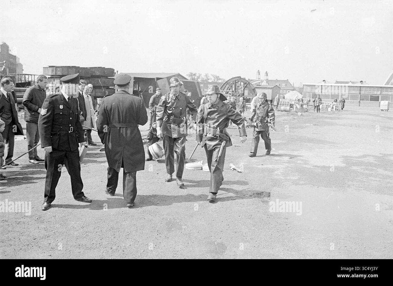 Dimostrazione dei vigili del fuoco, Figee, incendi, vigili del fuoco, 20-05-1967 Whizgle News, Dutch Desk, Paesi Bassi, 1950-2000 Un gruppo di forze dell'ordine in uniforme interagisce in un sito industriale, mentre persone in cerca e varie strutture popolano lo sfondo. La scena trasmette un senso di attività organizzata e ordine pubblico in un ambiente vivace. Foto Stock