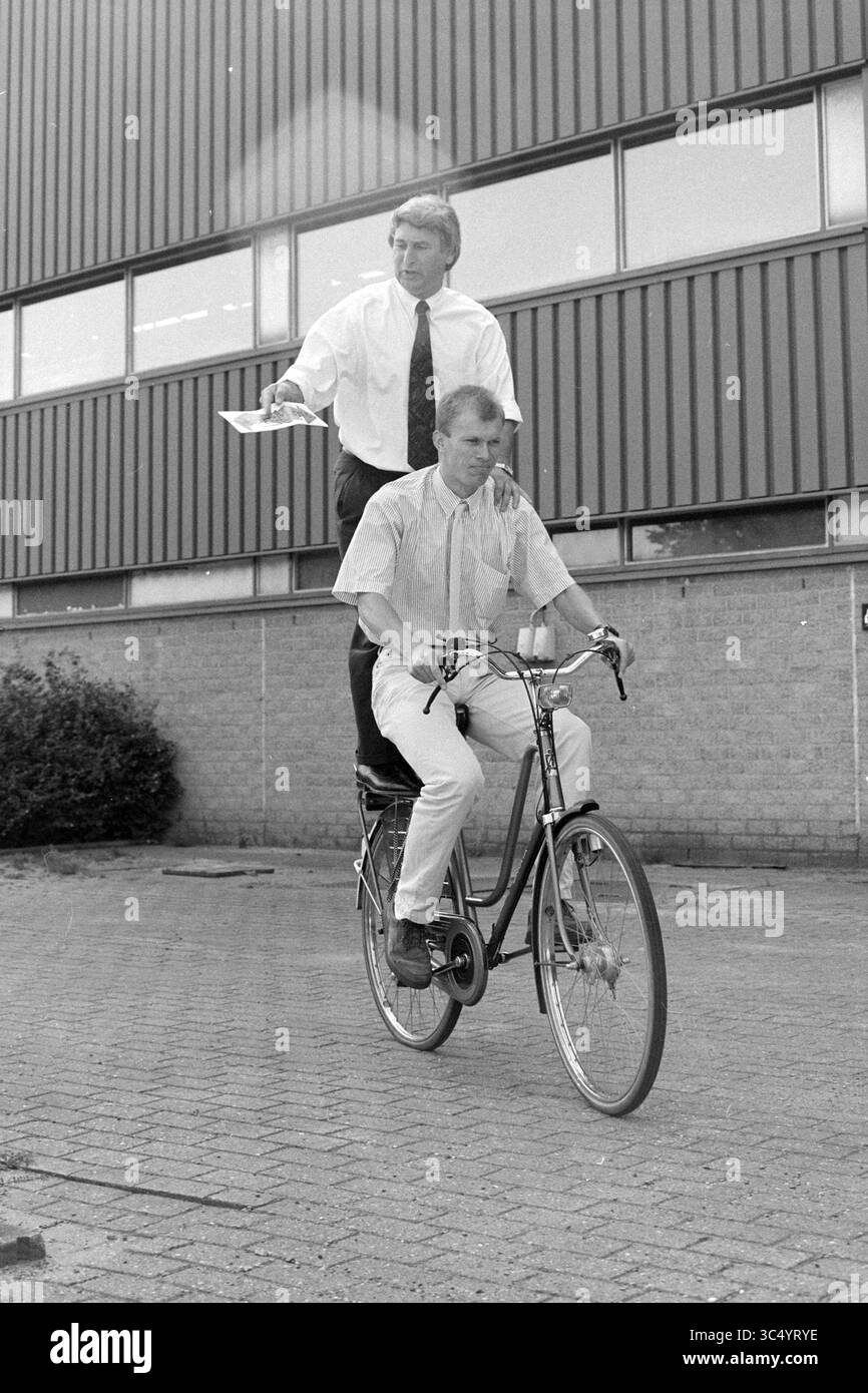 Coordinatori di consegna Haarlems Dagblad, 21-07-1992 Whizgle News, Dutch Desk, Paesi Bassi, 1950-2000 Un uomo in tuta si erge in cima a un altro uomo in bicicletta, tenendo fogli di carta, creando una scena umoristica e non convenzionale all'esterno di un edificio. Foto Stock