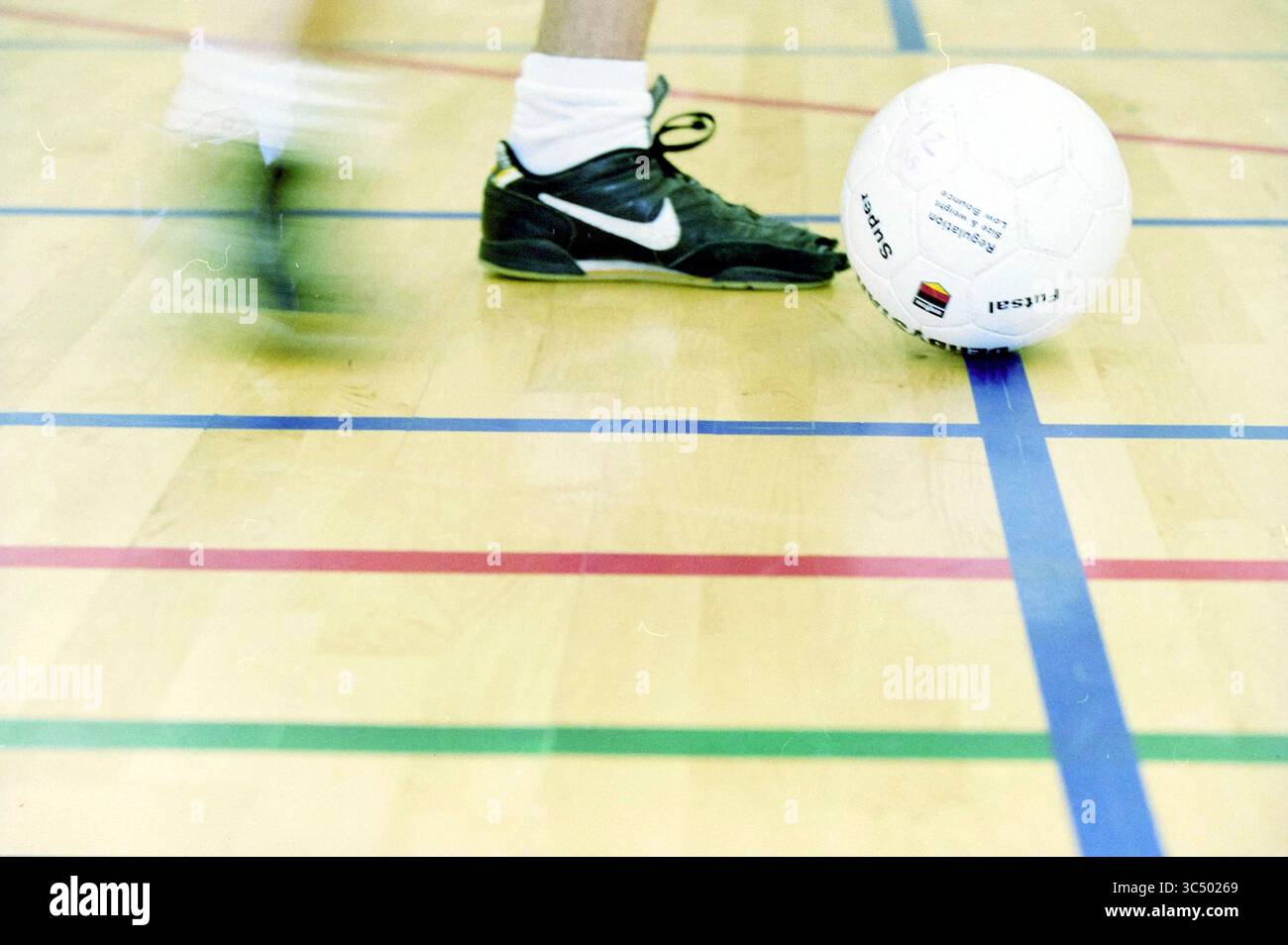 Indoor football Zandvoort, Zandvoort, 26-03-2002 Whizgle News, Dutch Desk, Paesi Bassi, 1950-2000 Un piede in movimento si avvicina a un pallone da calcio su un pavimento di palestra contrassegnato da linee colorate, suggerendo una partita attiva. Foto Stock