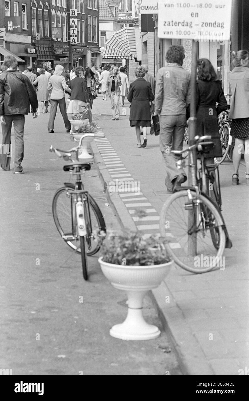 Scatole di fiori, Grote Houtstraat, Haarlem, Fiori e ragazze di fiori, Haarlem, Grote Houtstraat, Paesi Bassi, 17-07-1974 Whizgle News, Dutch Desk, Paesi Bassi, 1950-2000 Una vivace scena di strada piena di pedoni che passeggiano accanto ai negozi, mentre le biciclette sono parcheggiate nelle vicinanze accanto a una piantatrice unica. L'atmosfera cattura la vita quotidiana della città, con persone impegnate in varie attività e stili che riflettono l'epoca. Foto Stock