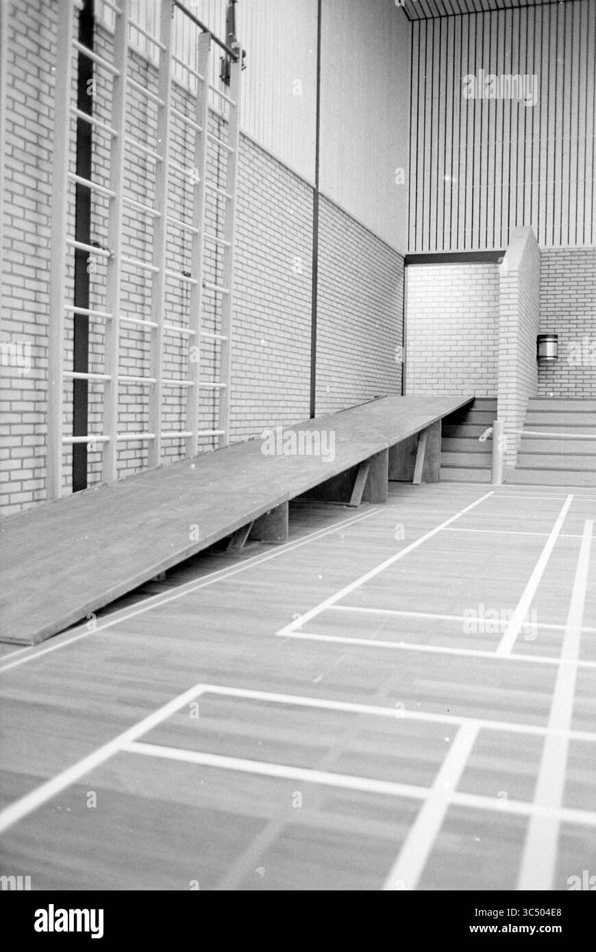 Int Nuovo centro sportivo IJmuiden, Sports Halls, IJmuiden, Paesi Bassi, 17-08-1979 Whizgle News, Dutch Desk, Paesi Bassi, 1950-2000 Una rampa di legno conduce dal pavimento a una piattaforma rialzata all'interno di una spaziosa palestra, caratterizzata da pareti in mattoni e un alto soffitto. L'area è caratterizzata da linee del pavimento tipiche delle attività sportive, creando un ambiente organizzato e funzionale. Foto Stock