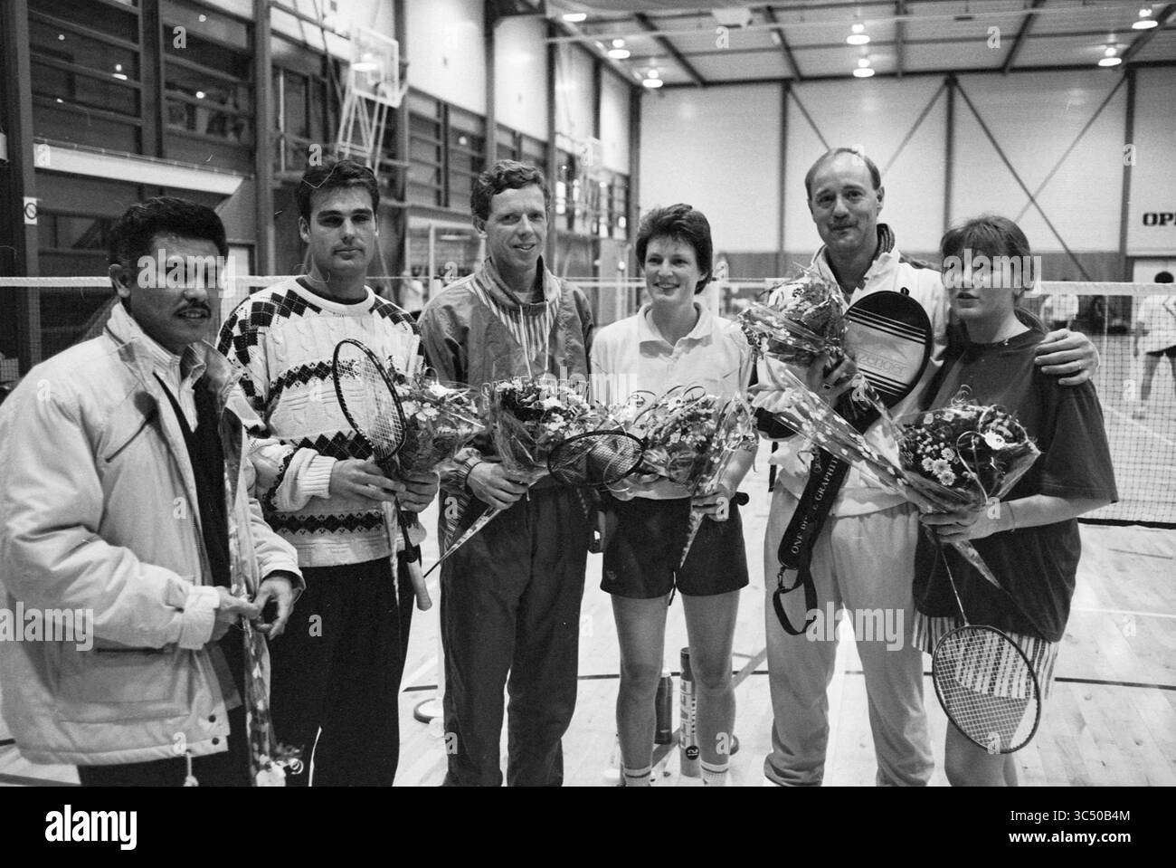 Badminton: Let IT Be Camp, 16-01-1993 Whizgle News, Dutch Desk, Paesi Bassi, 1950-2000 Un gruppo di sei persone si trova insieme in un luogo sportivo, ognuno con racchette da tennis e mazzi di fiori. Sembra che stiano celebrando un evento di successo, con sorrisi e un senso di cameratismo tra di loro. L'ambiente al coperto presenta campi da badminton sullo sfondo, suggerendo una riunione atletica. Foto Stock