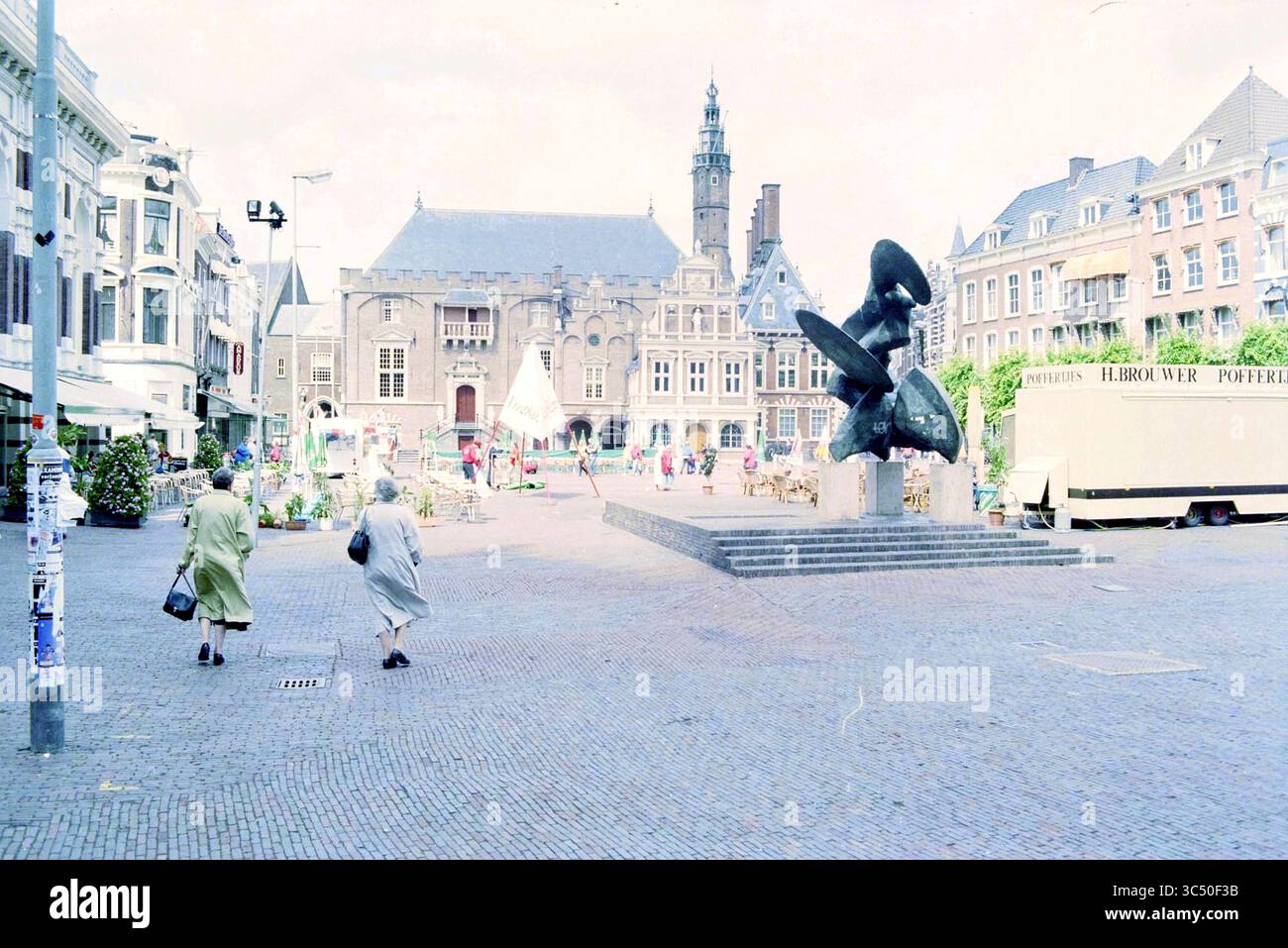 Grote Markt sunnier, Haarlem, Grote Markt, Paesi Bassi, 03-07-1996 Whizgle News, Dutch Desk, Paesi Bassi, 1950-2000 Una vivace piazza presenta una scultura di rilievo al centro, circondata da una vivace attività. Le persone passeggiano piacevolmente, con edifici storici e una torre dell'orologio sullo sfondo, creando un'atmosfera vivace e invitante. Bancarelle colorate e posti a sedere all'aperto suggeriscono un vivace mercato o un evento in corso. Foto Stock