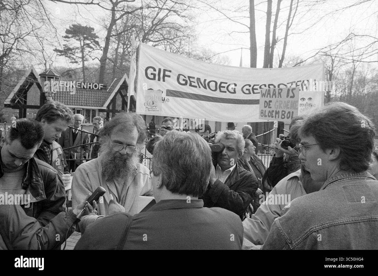 Protesta contro il veleno nei bulbi di fiori a Keukenhof, Lisse, Stationsweg, 01-04-1992 Whizgle News, Dutch Desk, i Paesi Bassi, 1950-2000 Persone si radunano intorno a oratori in occasione di una protesta, con discussioni mirate in corso. Un grande banner sullo sfondo esprime un messaggio audace, mentre i giornalisti e gli spettatori ascoltano con attenzione. La scena cattura un momento di attivismo e coinvolgimento del pubblico. Foto Stock