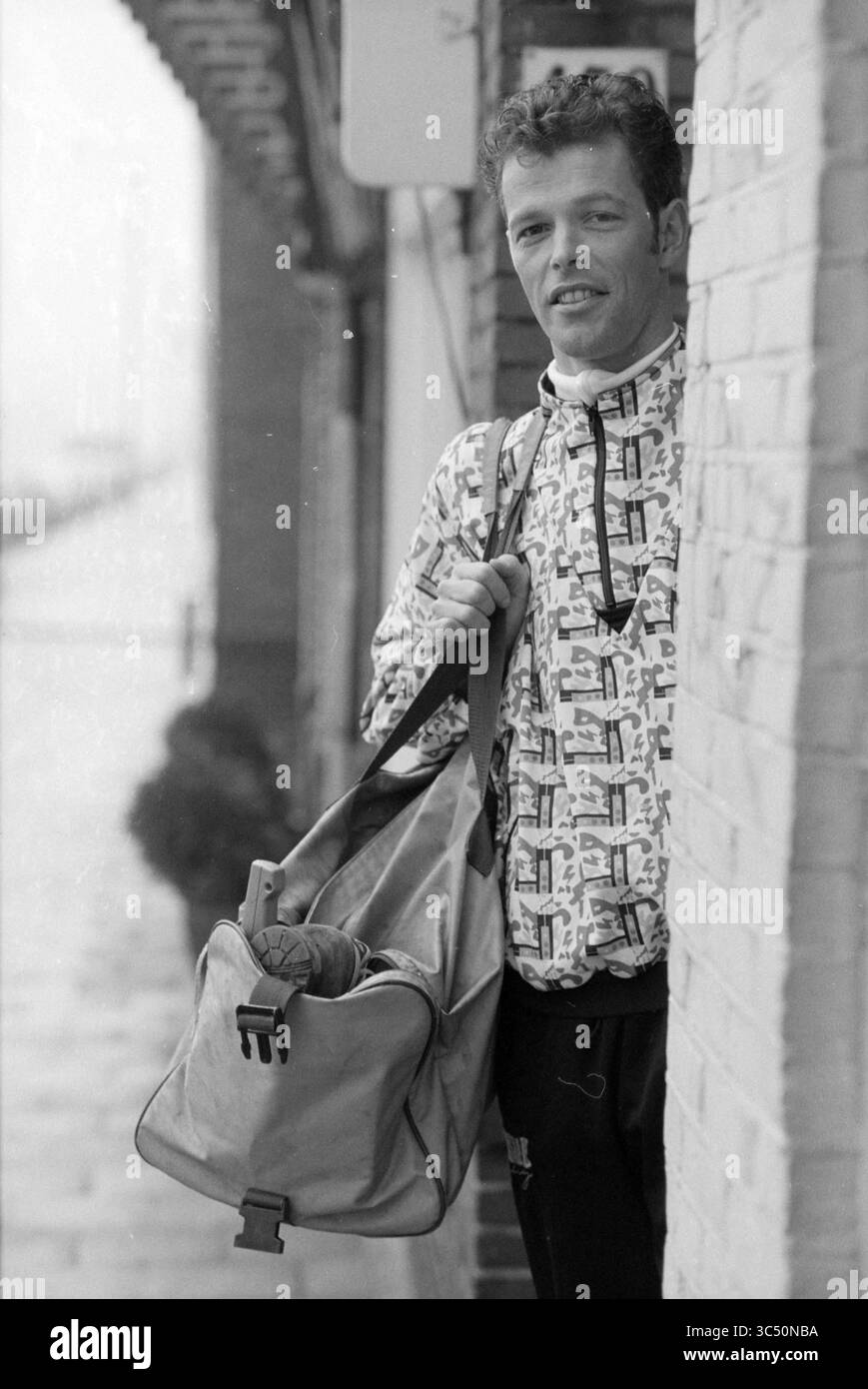 Gerard Kisting, allenatore, 18-01-1991 Whizgle News, Dutch Desk, Paesi Bassi, 1950-2000 Un giovane si appoggia contro un edificio, tenendo in mano una borsa sportiva sulla spalla. Indossa una giacca a motivi geometrici e mostra un comportamento sicuro ma rilassato, apparentemente pronto per un'avventura o un allenamento. Foto Stock