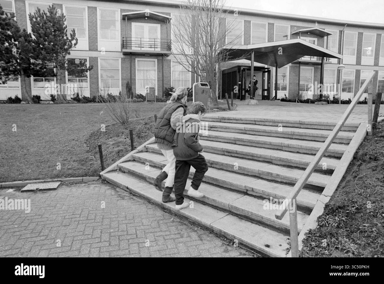 Open Day Leeuwenhorst College, Open Day e open House, 24-01-1990 Whizgle News, Dutch Desk, Paesi Bassi, 1950-2000 due bambini salgono una serie di gradini di pietra verso un grande edificio con ingresso coperto, delimitato da un'area erbosa e alberi. La scena cattura un momento di compagnia mentre si fanno strada insieme. Foto Stock