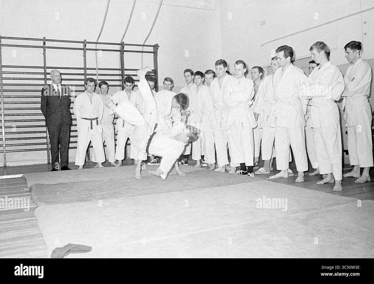 Lezioni di judo per polizia, polizia, 19-04-1968 Whizgle News, Dutch Desk, Paesi Bassi, 1950-2000 Un gruppo di individui vestiti con uniformi di arti marziali osserva una dimostrazione in uno spazio di allenamento, dove un praticante esegue un lancio mentre un altro è a mezz'aria. Un istruttore o una figura autoritaria si trova di fianco, osservando la scena mentre gli altri studenti guardano attentamente la tecnica messa in mostra. Foto Stock