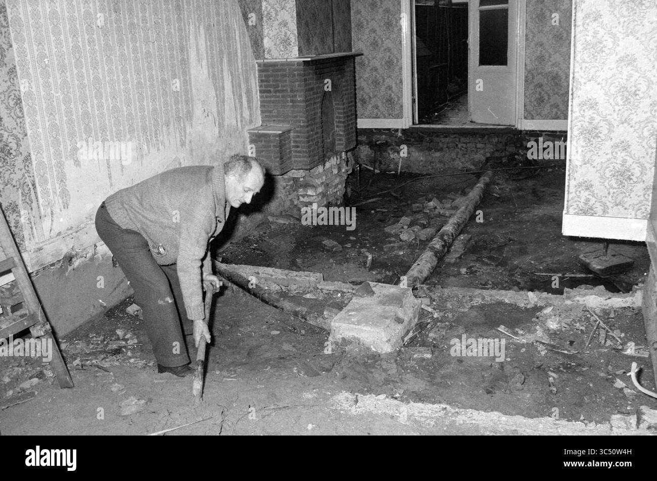 Riparazione Fondazione Oude Amsterdamsebuurt, quartieri, centri comunali, negozi locali, centri di formazione, Renovation, Haarlem, Paesi Bassi, 02-02-1984 Whizgle News, Dutch Desk, i Paesi Bassi, 1950-2000 un uomo anziano si inginocchia a terra, usando uno strumento per scavare o fare leva sul pavimento in una stanza che mostra segni di ristrutturazione. Le travi esposte e un caminetto parzialmente smantellato indicano un cambiamento strutturale significativo, mentre la carta da parati a motivi aggiunge uno sfondo contrastante alla scena. Foto Stock