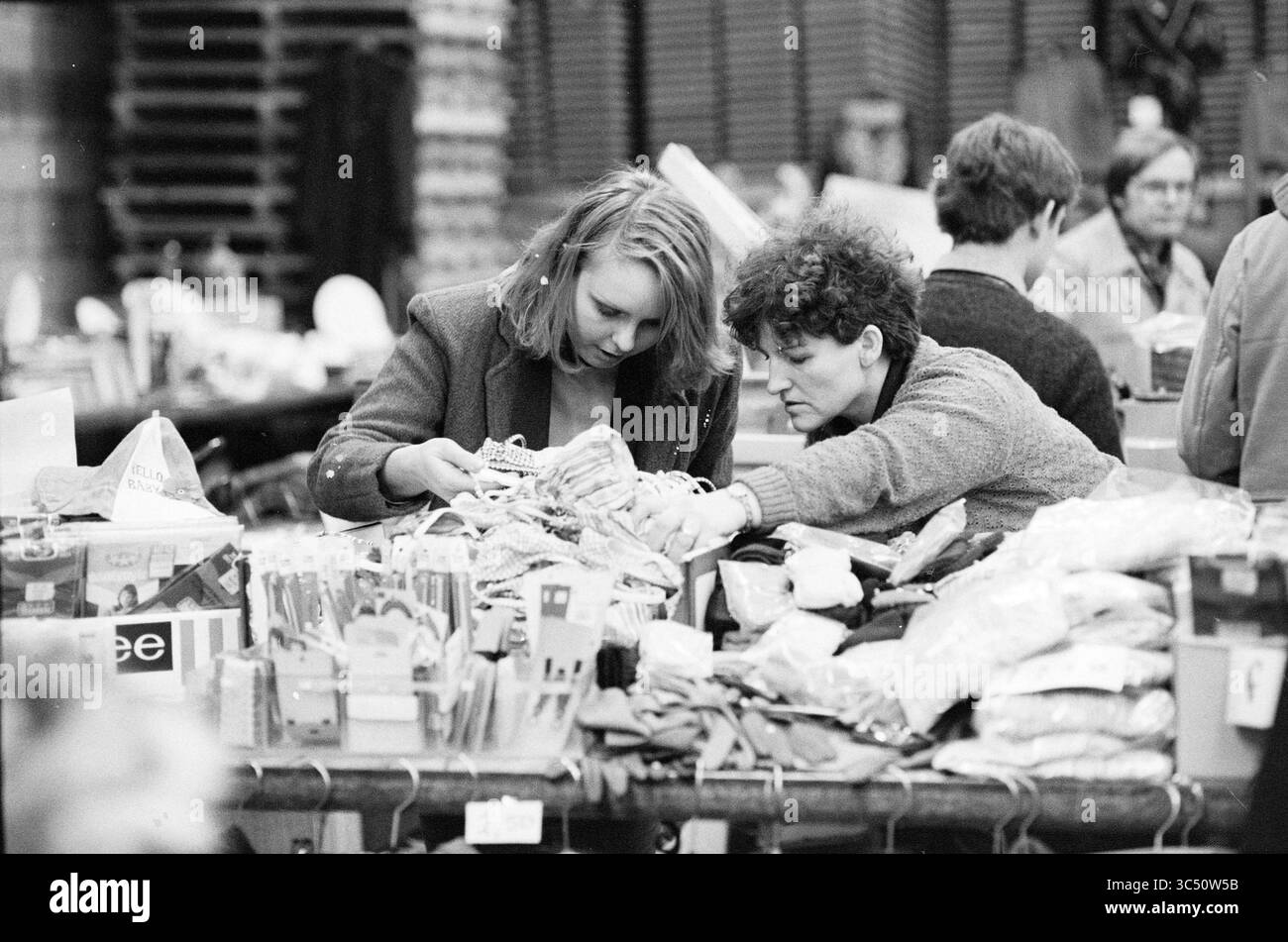 Report Black Market Beverwijk, Market, 00-00-1981 Whizgle News, Dutch Desk, Paesi Bassi, 1950-2000 due donne stanno esaminando attentamente gli oggetti in un vivace mercato, circondato da vari beni e dalla vivace atmosfera di chi ama fare shopping nelle vicinanze. Foto Stock