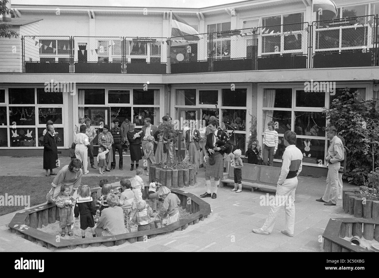 50 anni, asilo nido, Haarlem, Giubileo, anniversari, Haarlem, paesi Bassi, 15-06-1985 Whizgle News, Dutch Desk, Paesi Bassi, 1950-2000 Una scena vivace in un parco giochi pieno di bambini di varie età impegnati in attività ludiche. Gli adulti supervisionano mentre i bambini esplorano un'area giardino circondata da un edificio moderno con grandi finestre. Alcuni bambini si radunano intorno a una fossa di sabbia, mentre altri interagiscono con i colleghi nelle vicinanze, creando un'atmosfera vibrante di gioco e cameratismo. Foto Stock