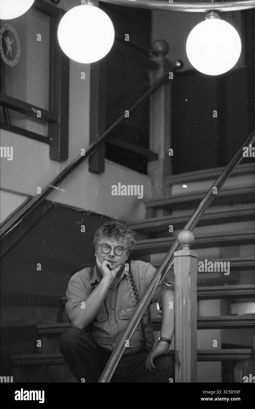Boulangé, presentatore Lingo, 26-05-1993 Whizgle News, Dutch Desk, Paesi Bassi, 1950-2000 Un individuo premuroso siede su una scala, sporadicamente appoggiato contro la ringhiera, con un accenno di contemplazione nella loro espressione. Le lampade rotonde sono appese sopra, emettendo una luce soffusa sullo sfondo, migliorando l'atmosfera dello spazio. Foto Stock