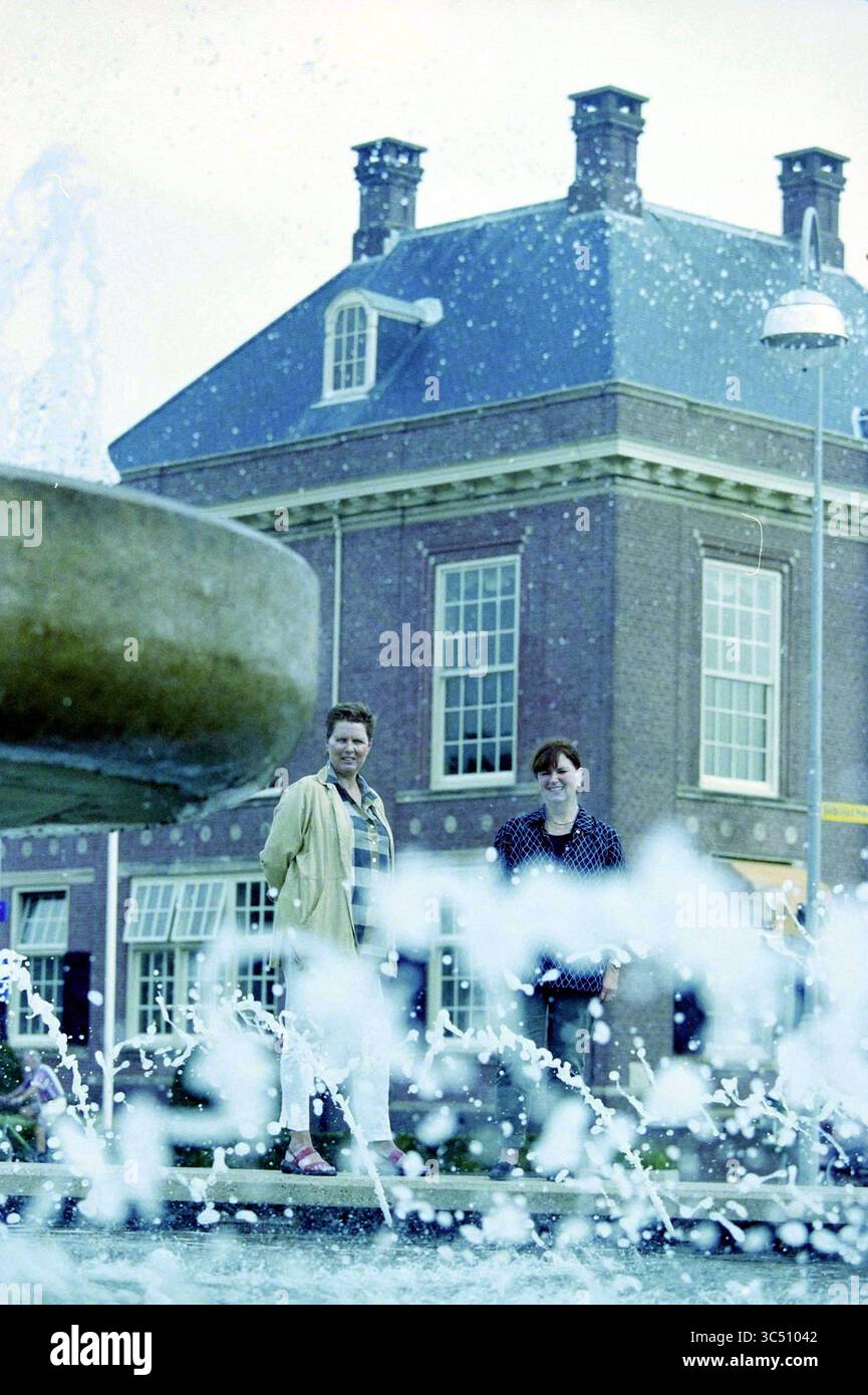 Due donne di fronte a un vecchio edificio Whizgle News, Dutch Desk, Paesi Bassi, 1950-2000 due persone si trovano vicino a una fontana, con acqua che spruzza giocosamente intorno a loro sullo sfondo di un edificio signorile. L'atmosfera cattura un momento di tranquillità e svago. Foto Stock