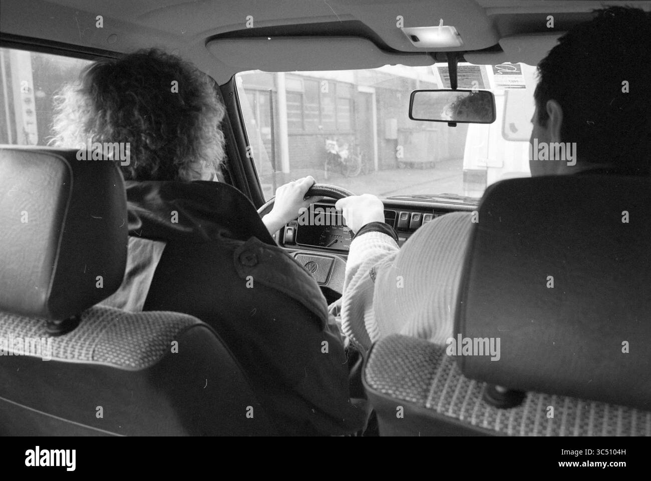 Donna in macchina, lezione di guida? Whizgle News, Dutch Desk, Paesi Bassi, 1950-2000 due persone sono sedute in un veicolo, con una persona concentrata sulla guida mentre l'altra osserva con attenzione. Gli interni sono accoglienti e presentano un cruscotto e specchi laterali, per un viaggio informale o quotidiano. Foto Stock