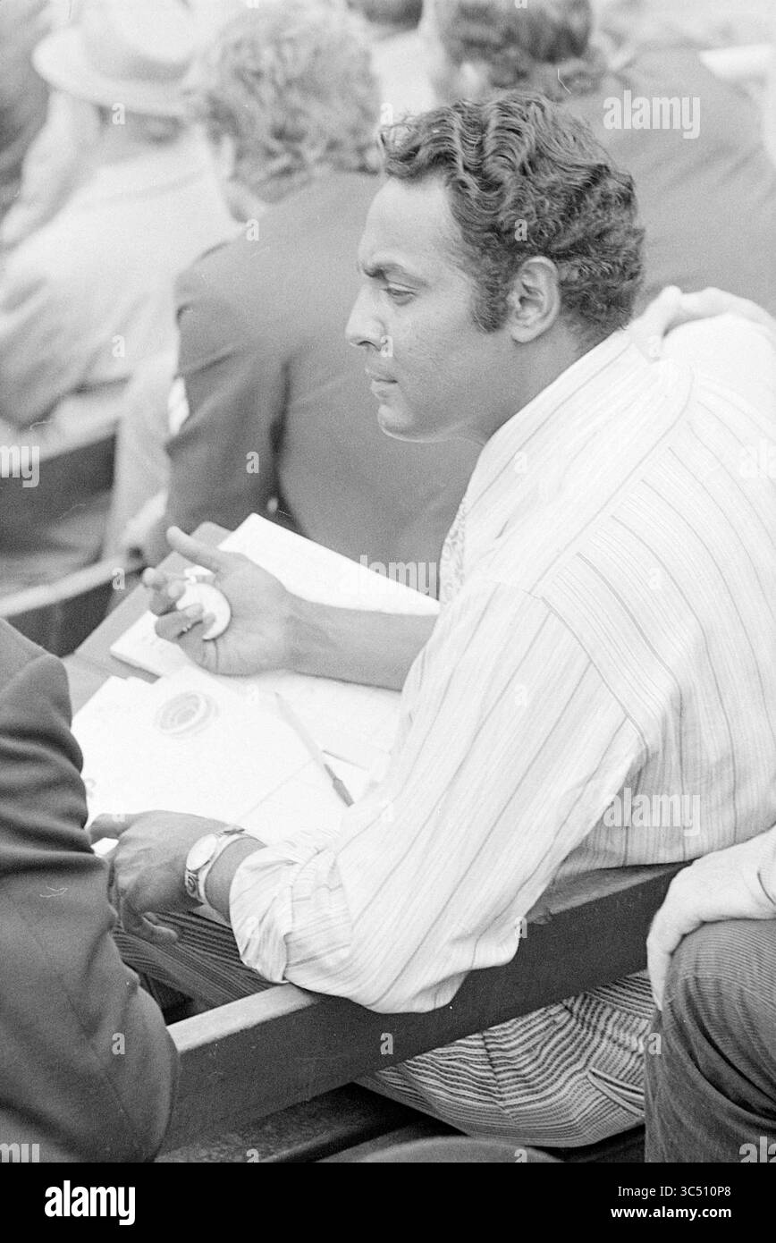 Nicaragua - Goldpanners, scout americano, Cuba - Sullivans, baseball, 06-07-1972 Whizgle News, Dutch Desk, Paesi Bassi, 1950-2000 Un uomo siede con attenzione, tenendo una penna e un taccuino, nel profondo del pensiero mentre osserva l'ambiente circostante. È vestito con una camicia a righe chiare, con un'espressione focalizzata sul suo viso, circondato da uno sfondo sfocato di persone in un ambiente all'aperto. Foto Stock